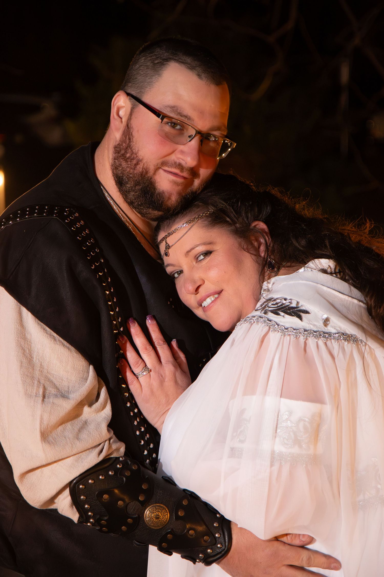 Couple in medieval wedding attire embrace romantically at night outdoor ceremony.