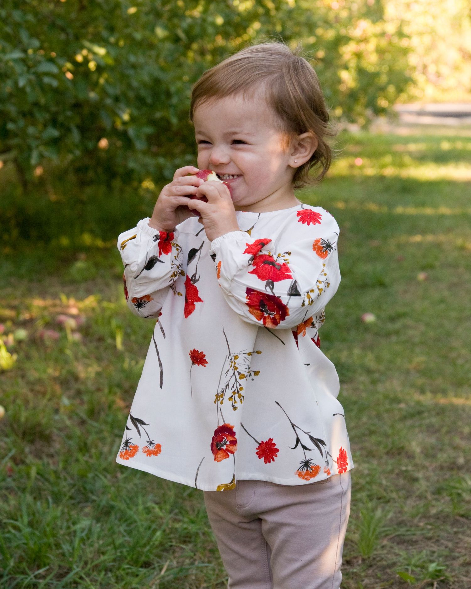 Happy toddler girl in floral dress laughing while playing outdoors in green park setting.