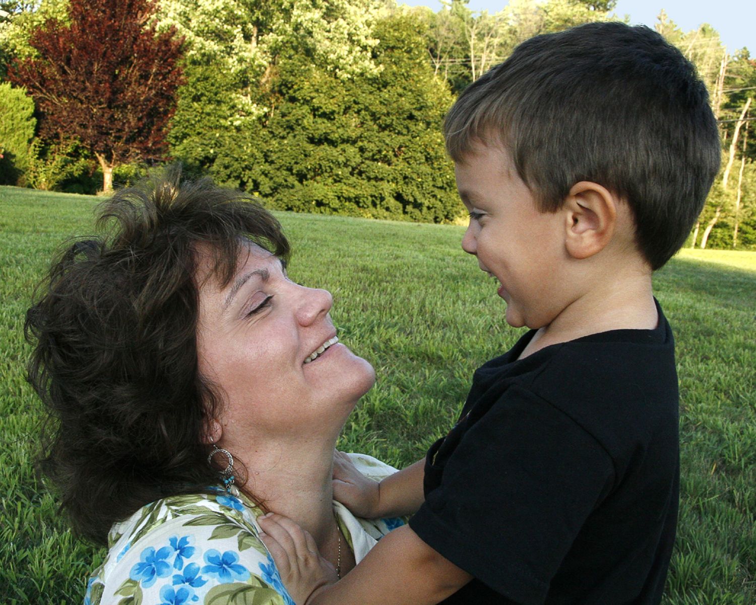 Grandmother and young boy share a joyful laughing moment together on a green lawn outdoors.