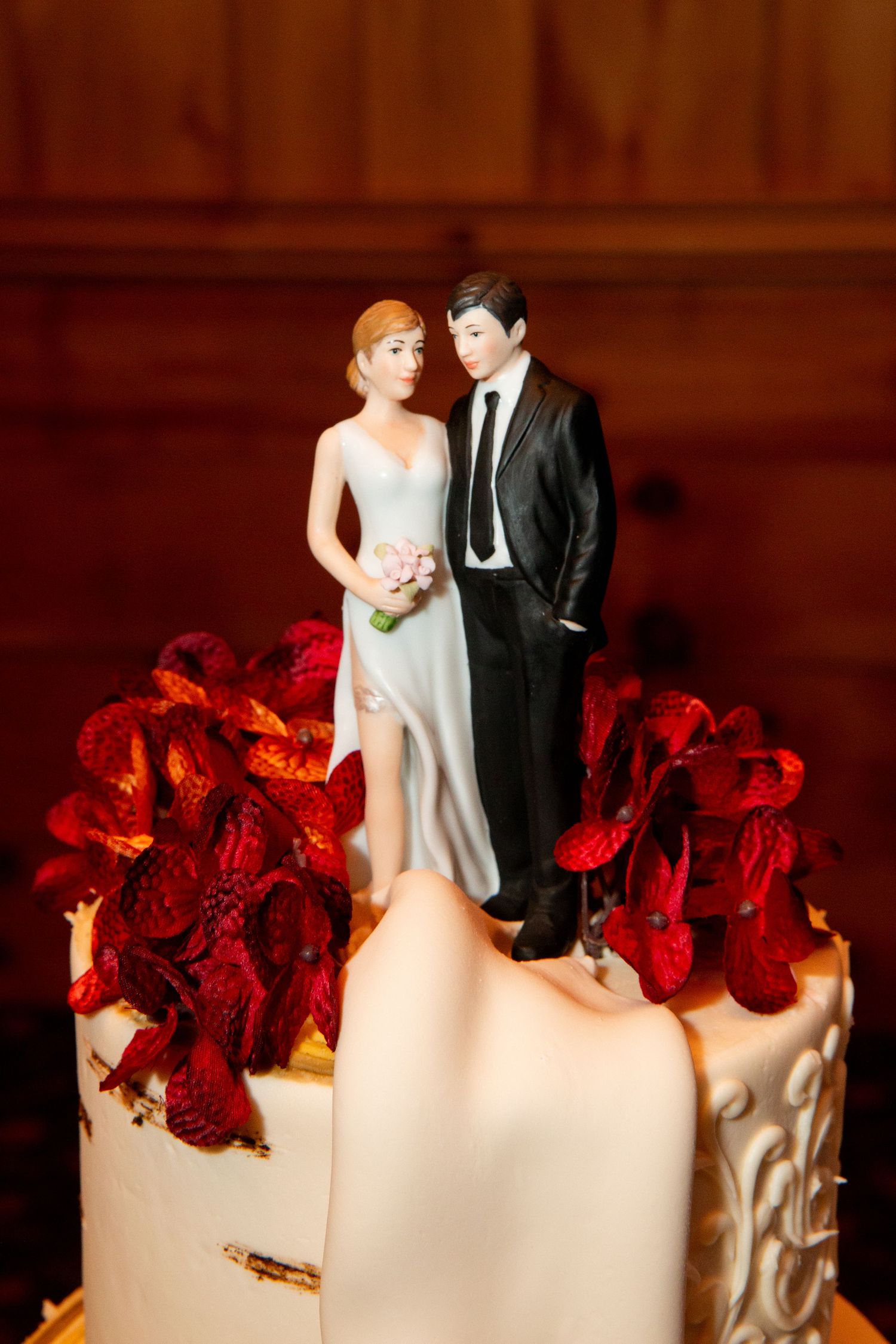 Classic bride and groom cake topper surrounded by red flowers on white wedding cake.
