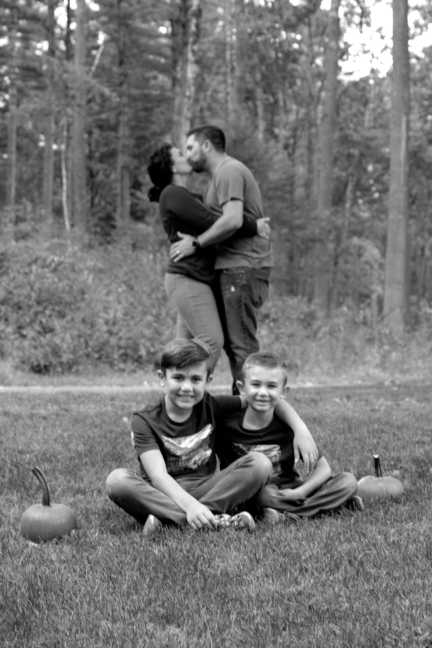 Black and white family photo with two boys sitting while parents kiss behind them.