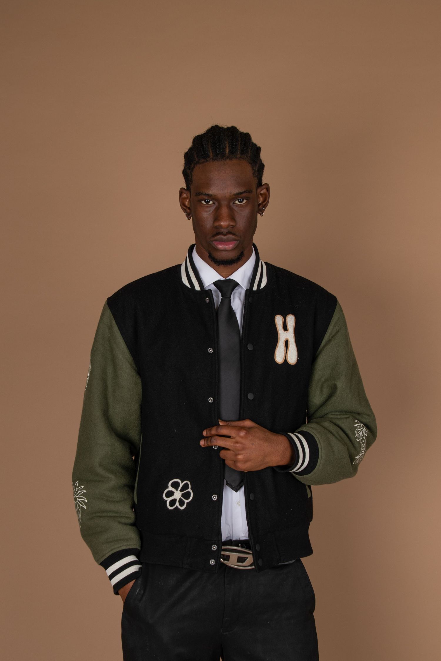 Stylish varsity jacket in black and olive green photographed against warm brown background.