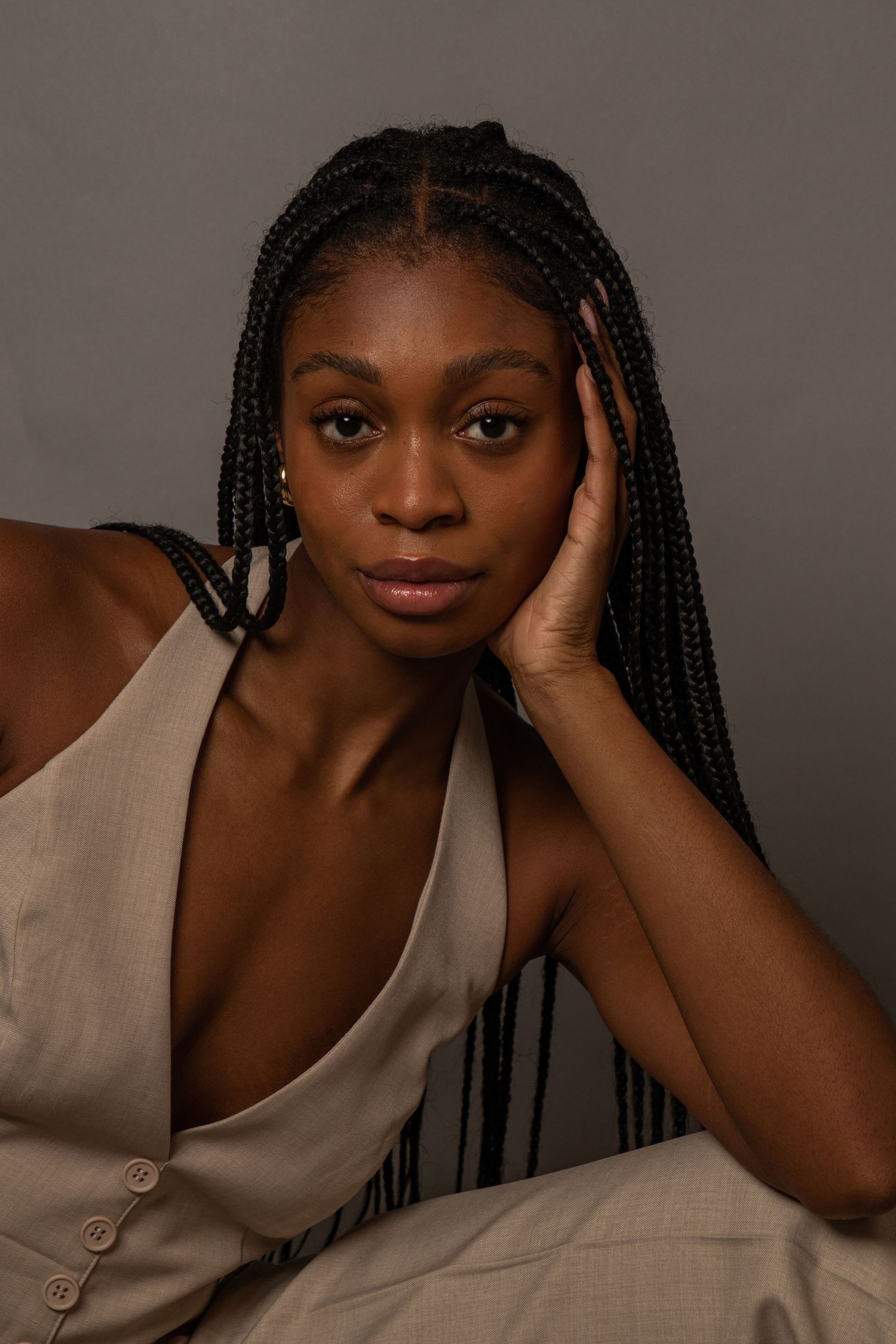 Artistic portrait with braided hair against neutral background in natural lighting.