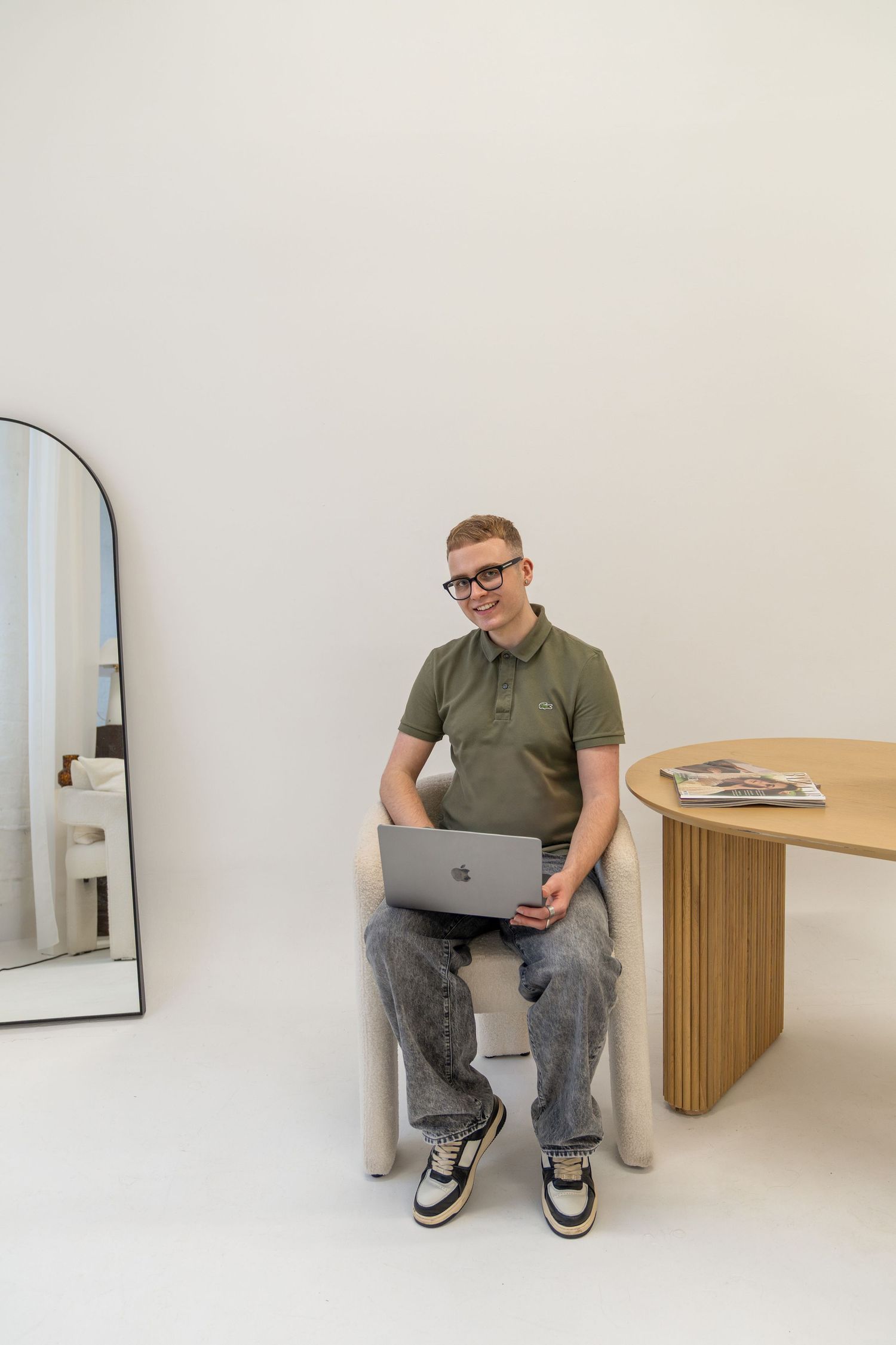 Person working on laptop in minimalist white room with floor mirror.