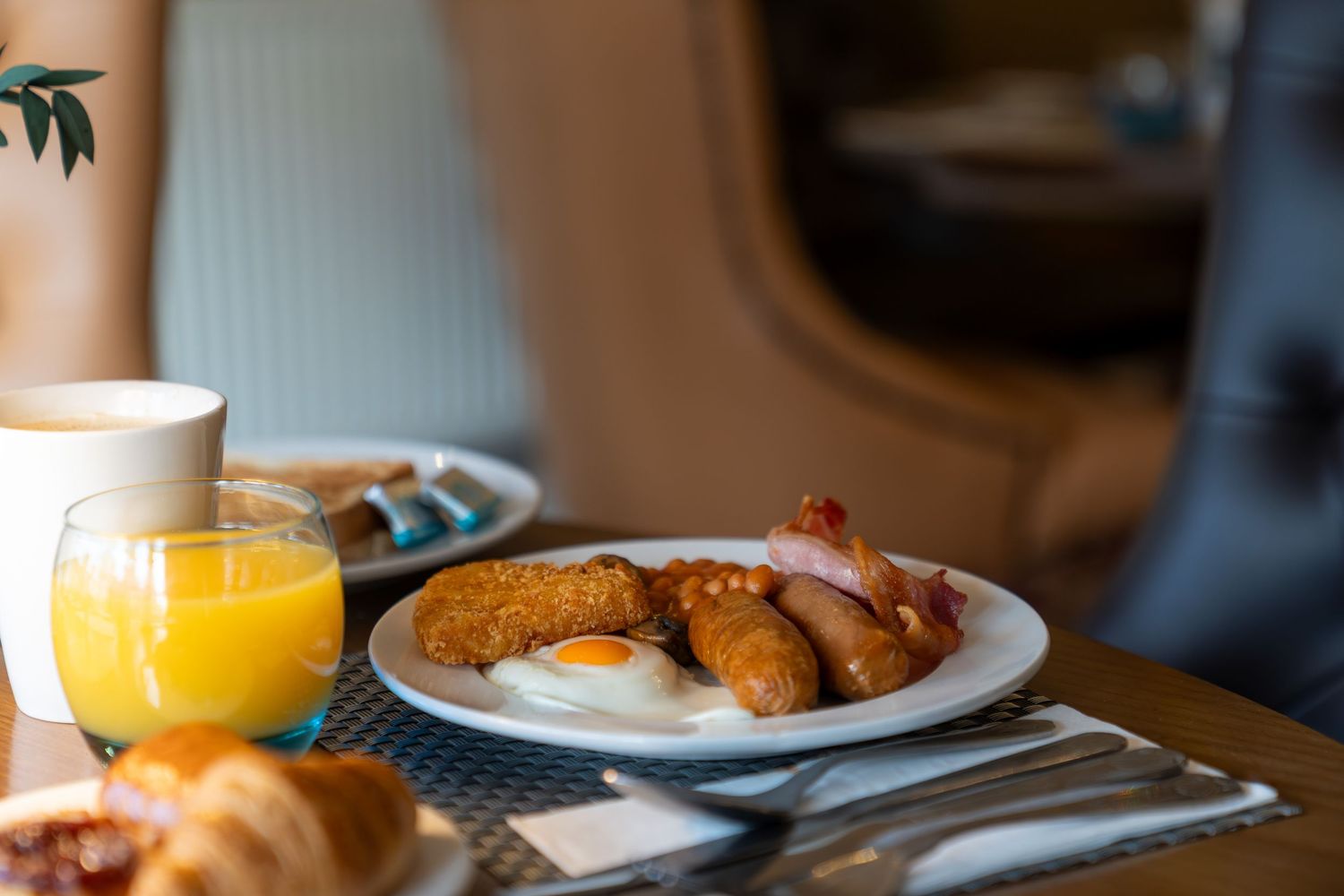 First class airplane breakfast with fried eggs, sausages, bacon, hash browns, and a glass of fresh orange juice.