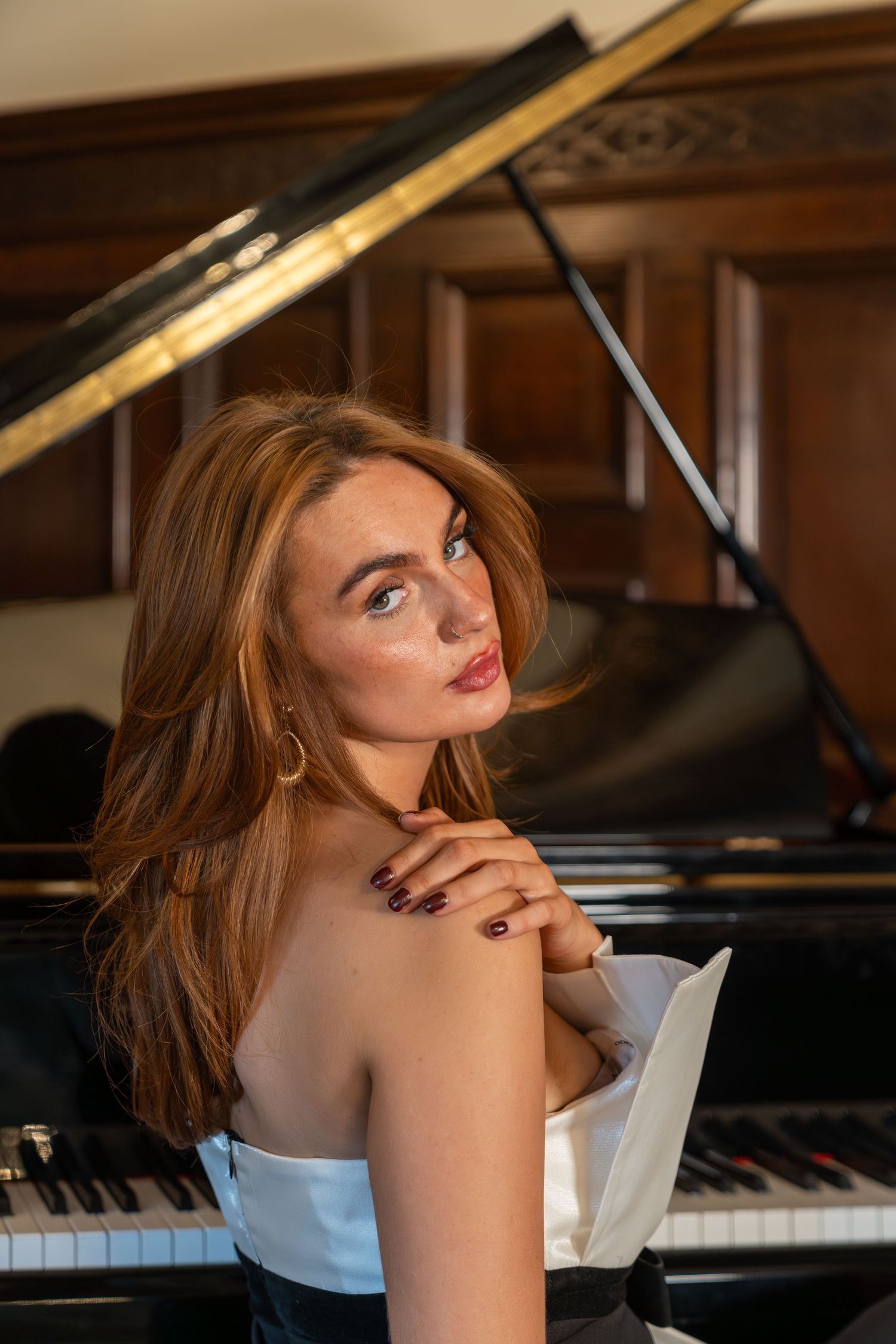 Elegant portrait by grand piano in formal dress with soft lighting.