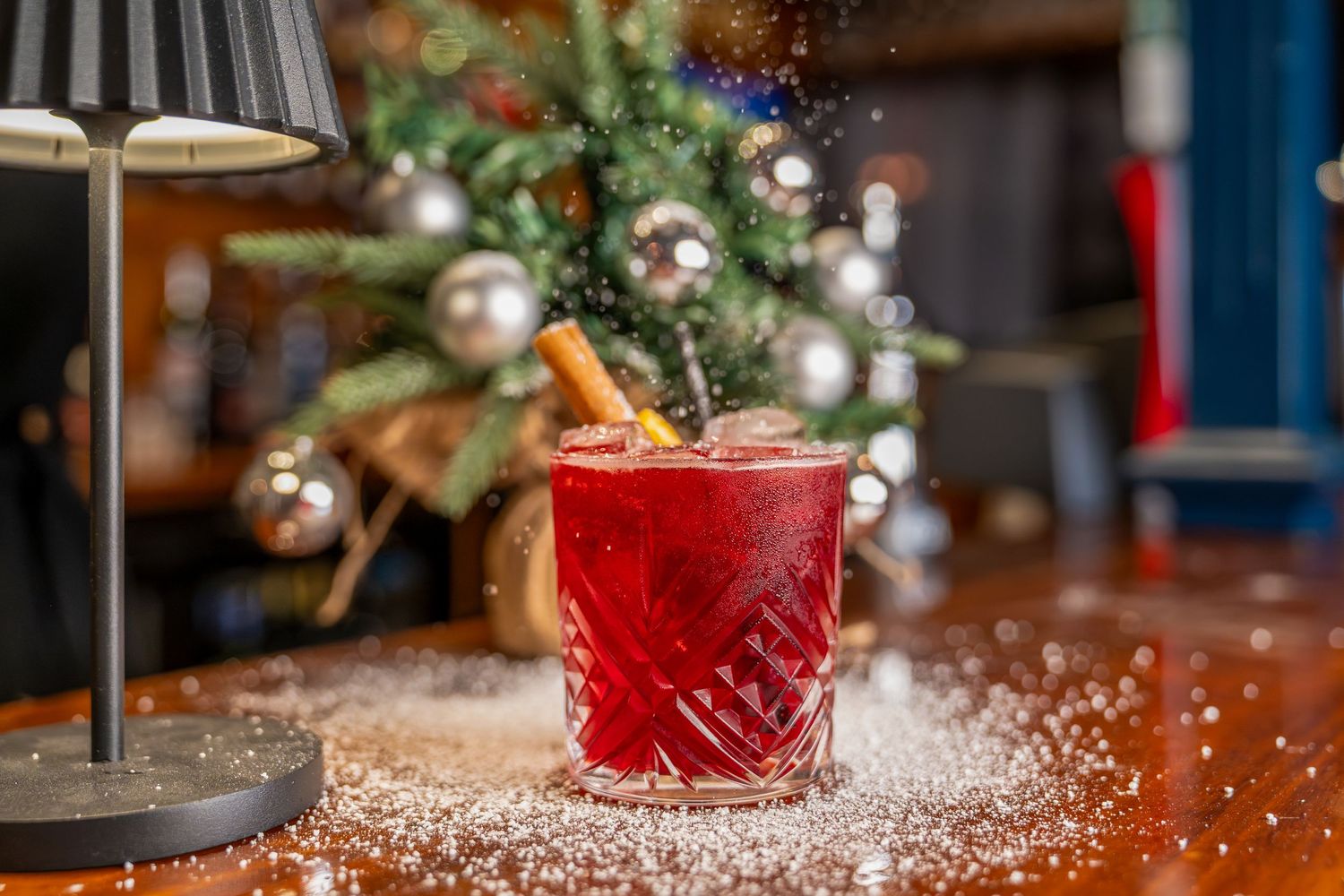 Festive Christmas table setting with red candles, pine branches, and sparkling snow-like decorations in warm lighting.