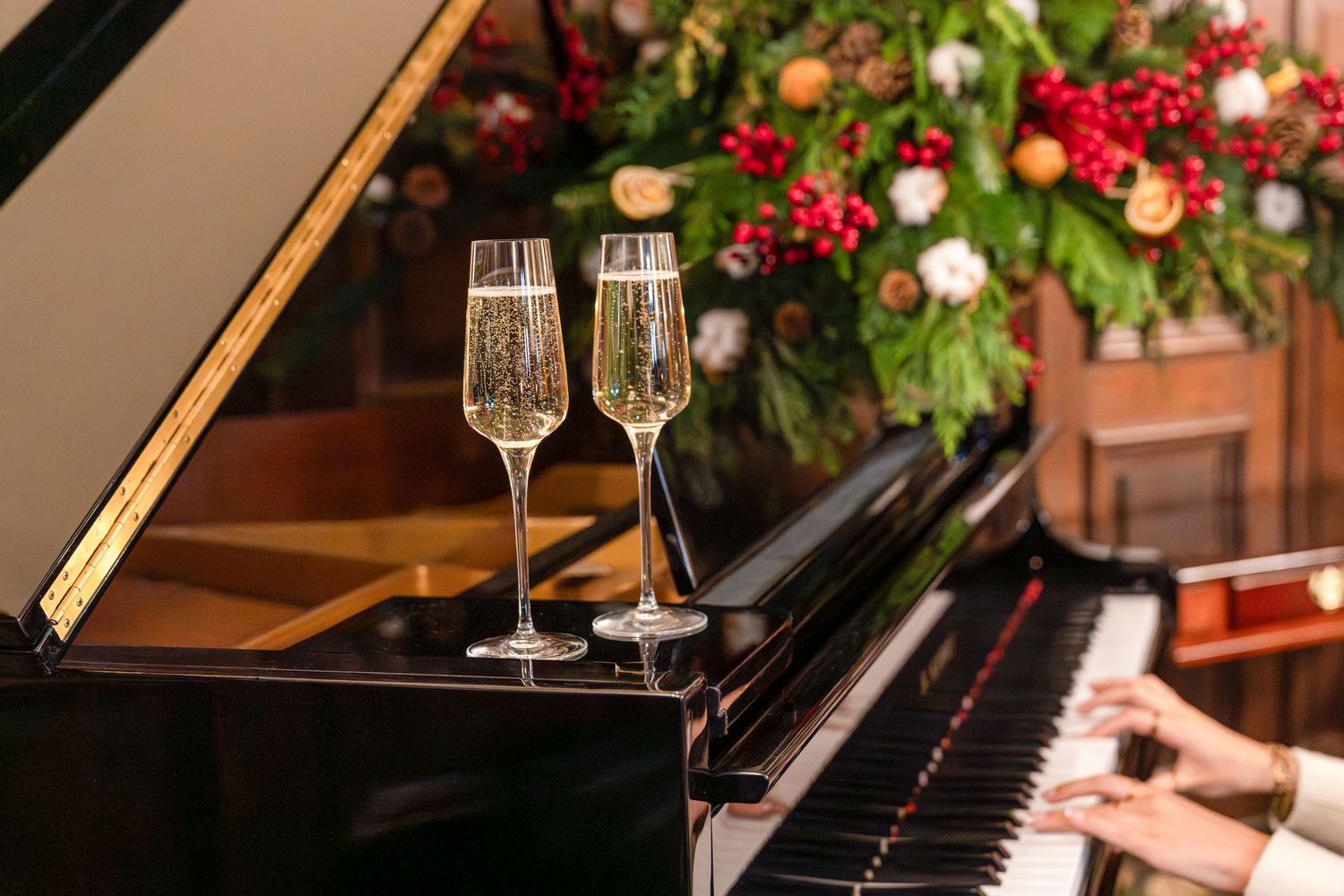 Two champagne flutes sit elegantly beside a grand piano adorned with romantic red and white floral arrangements.