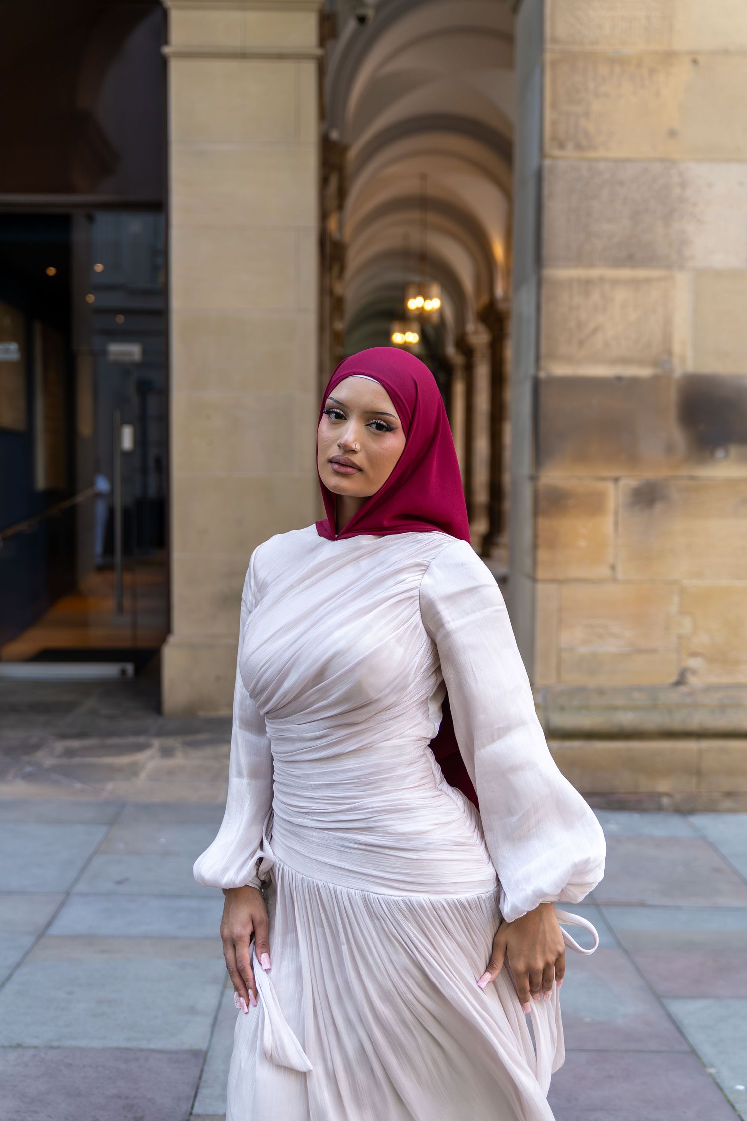 White pleated dress with balloon sleeves against stone archway architecture.