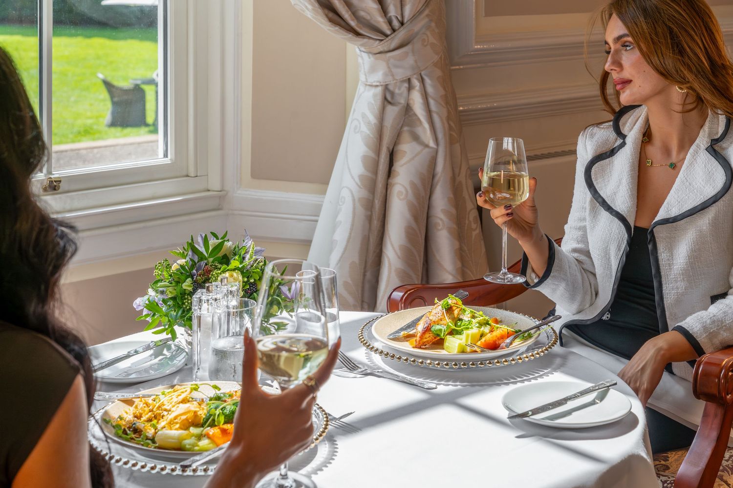 Two people enjoying an elegant lunch with wine and salads in a bright dining room.