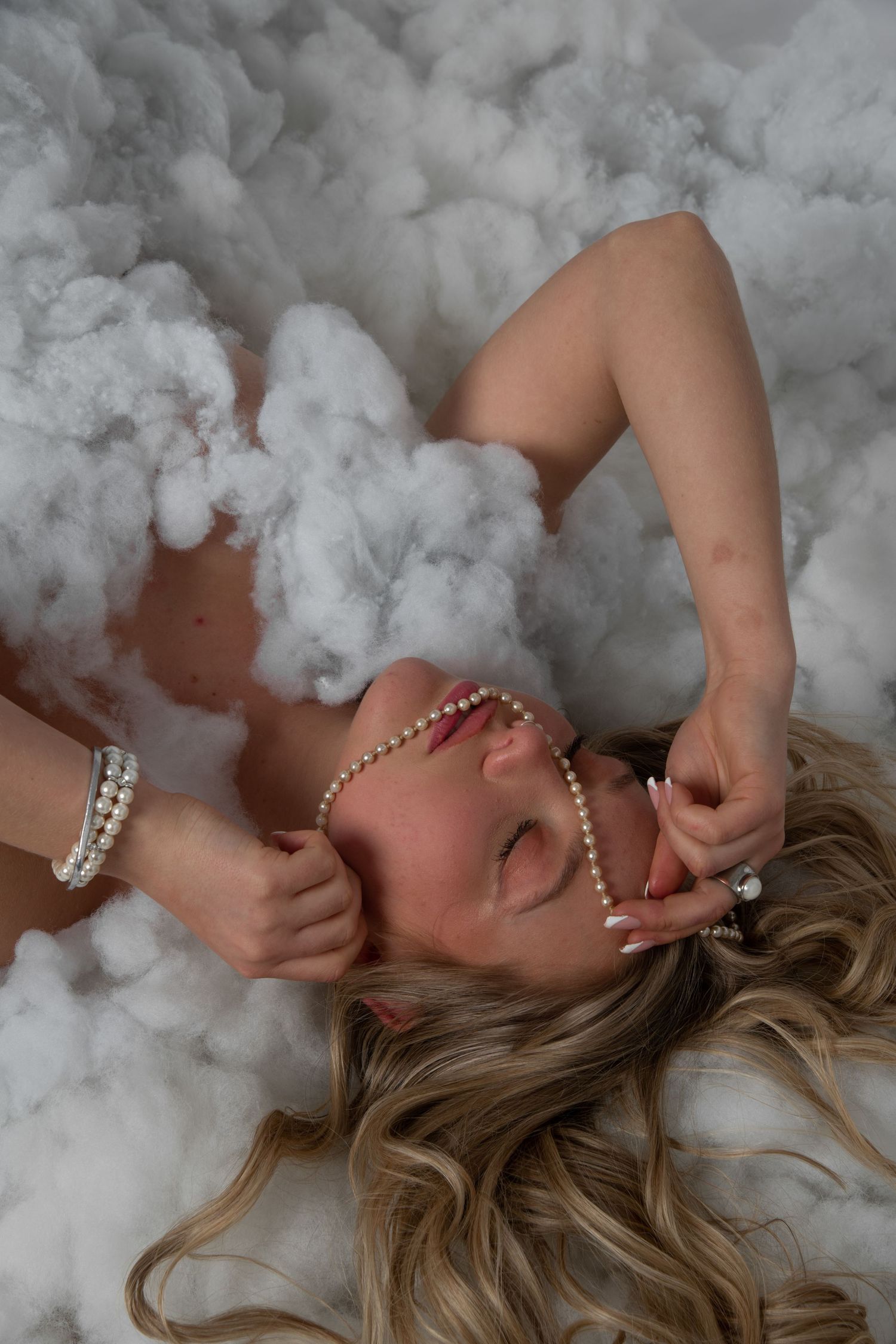 A dreamy portrait of someone lying in clouds of white cotton with pearl accessories.