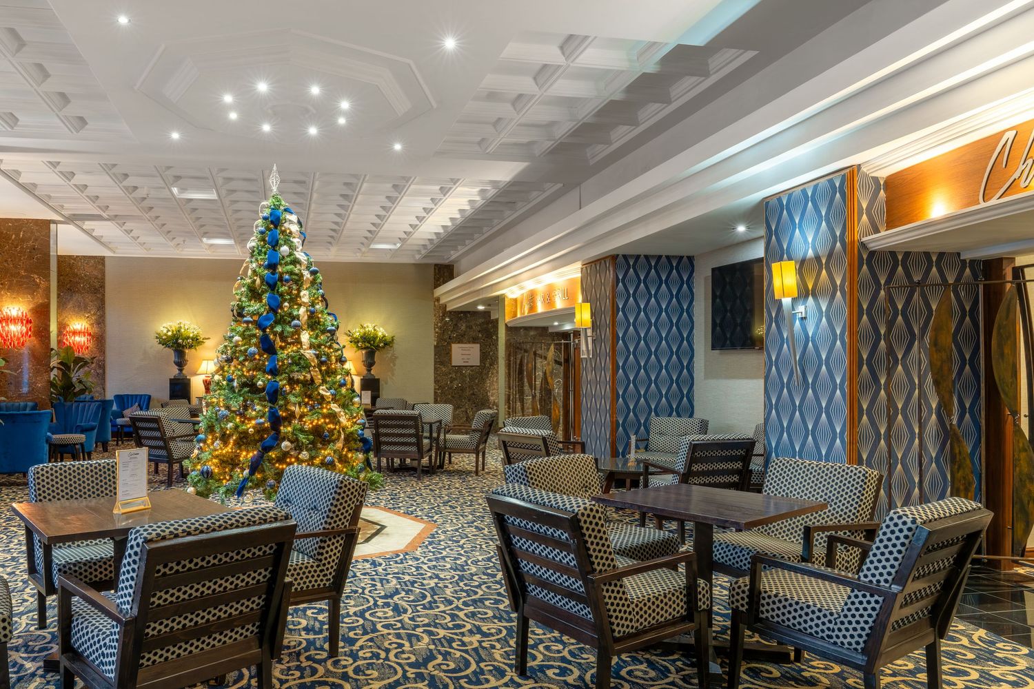 Panoramic view of an elegant hotel lobby decorated for Christmas with blue and gold accents and twinkling lights.