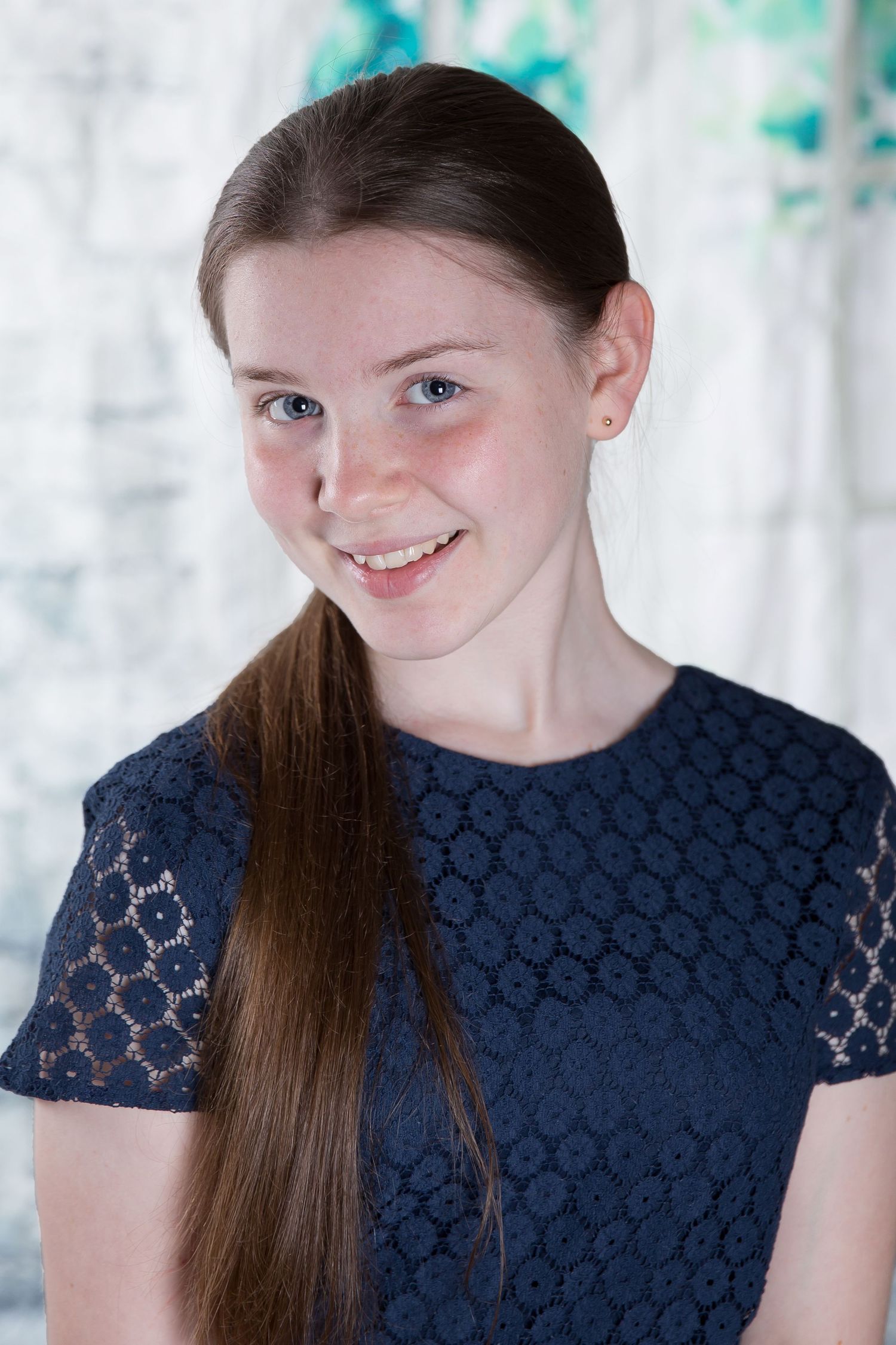 A young person wearing a navy blue lace dress smiles warmly while posing against a light background.