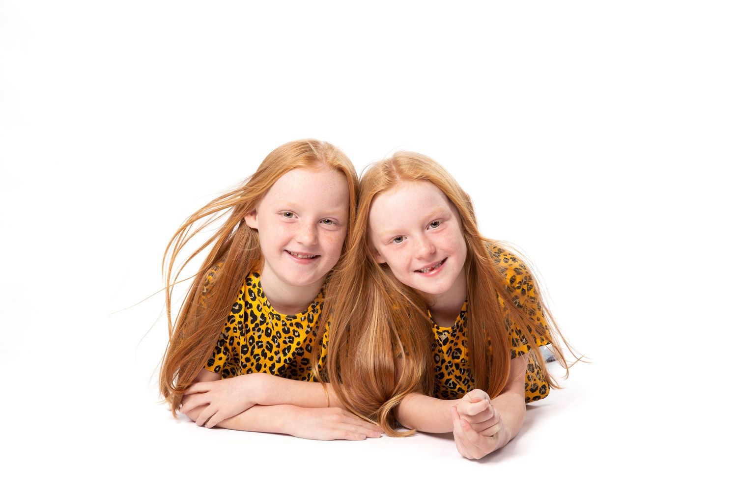 Three similar photos show two children with long blonde hair laying down and posing together for a portrait.