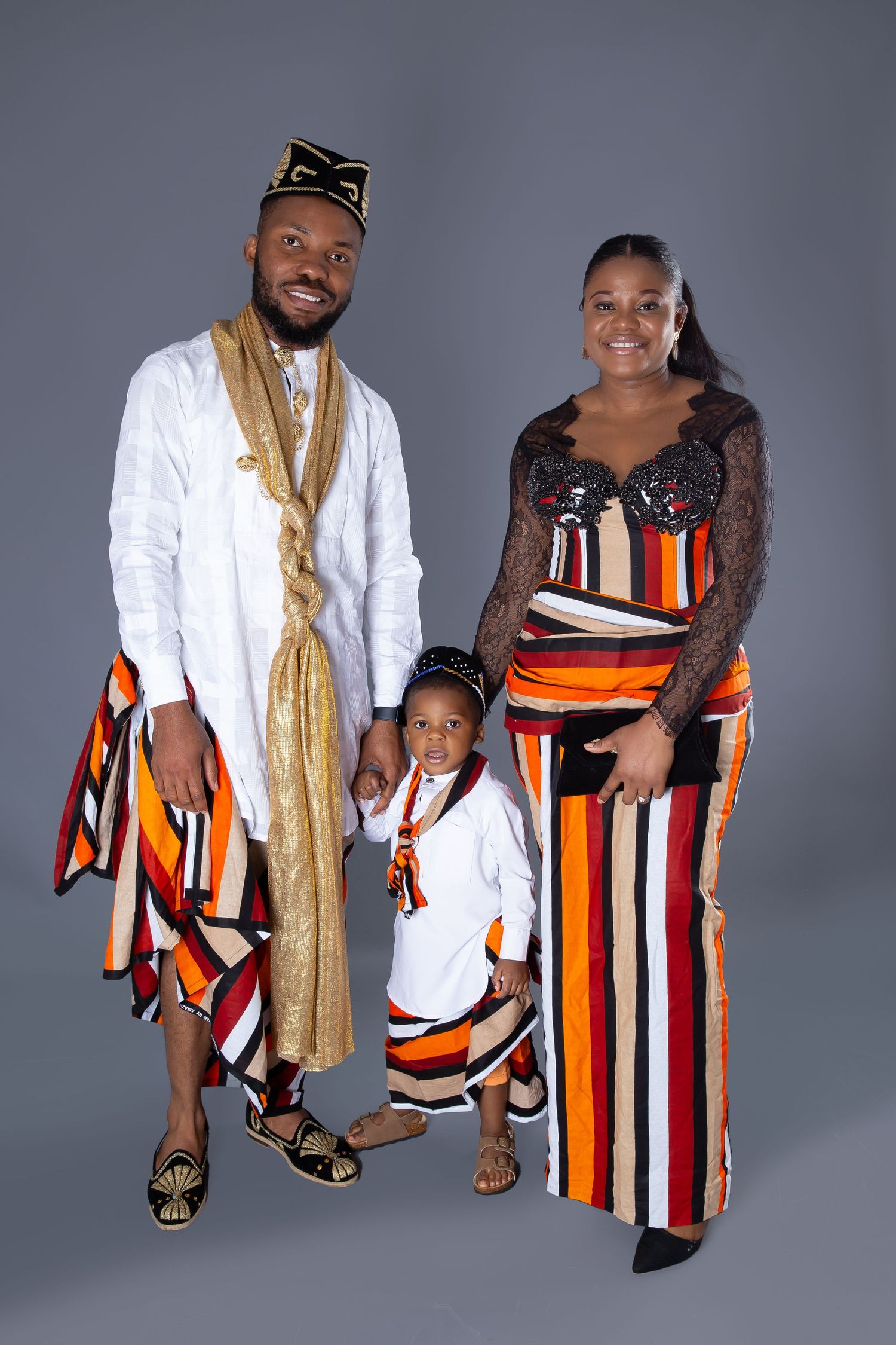 Family wearing matching striped orange, white and black African-inspired outfits poses together against grey background.