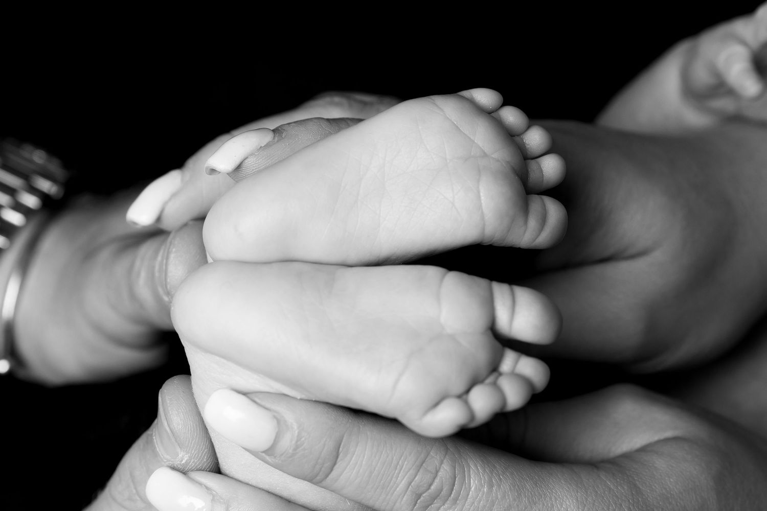 Four black and white photos showcasing gentle hand-holding moments between an adult and baby feet.