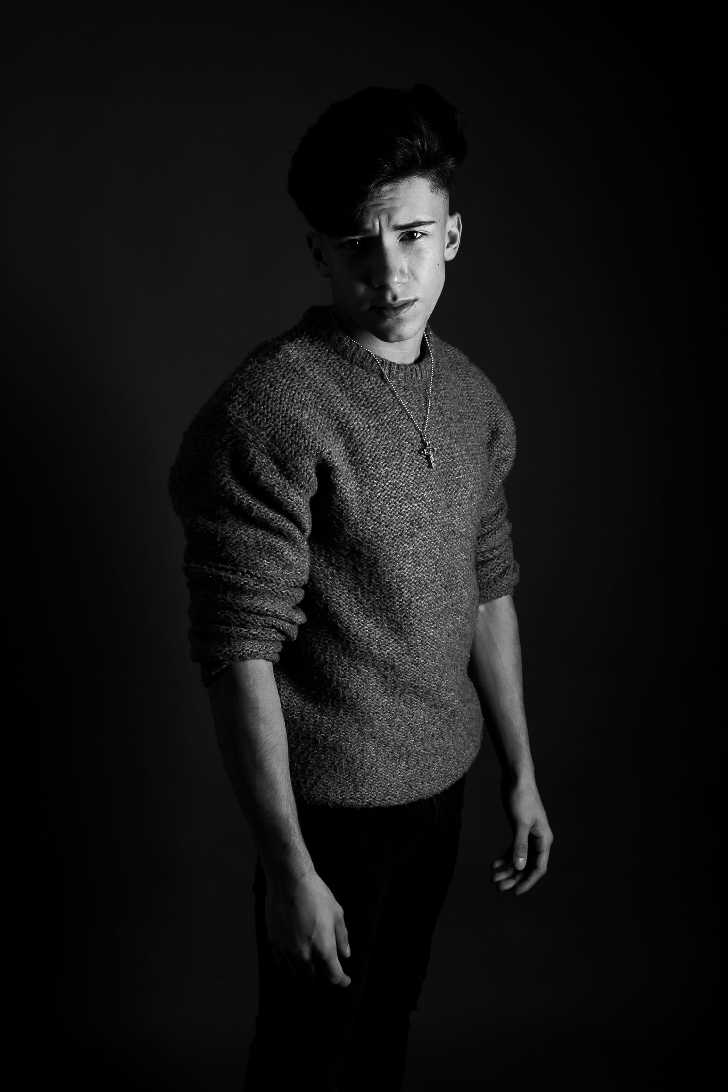 Dramatic black and white portrait of person in sweater against dark background with moody lighting.