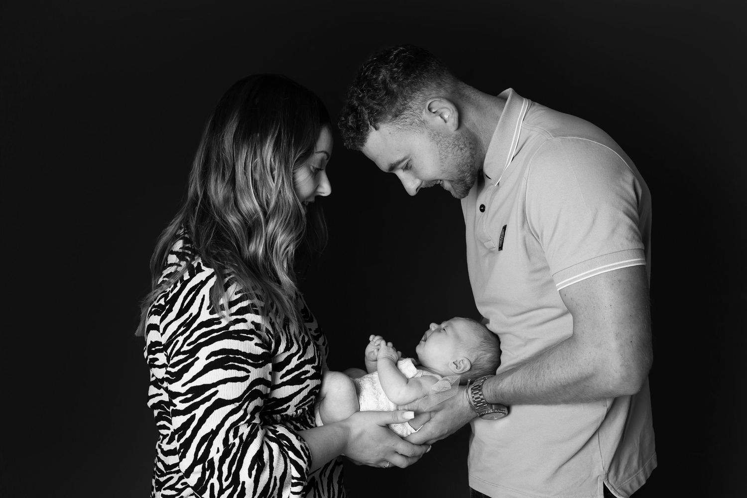 Black and white photo of couple tenderly holding and gazing at their newborn baby together.