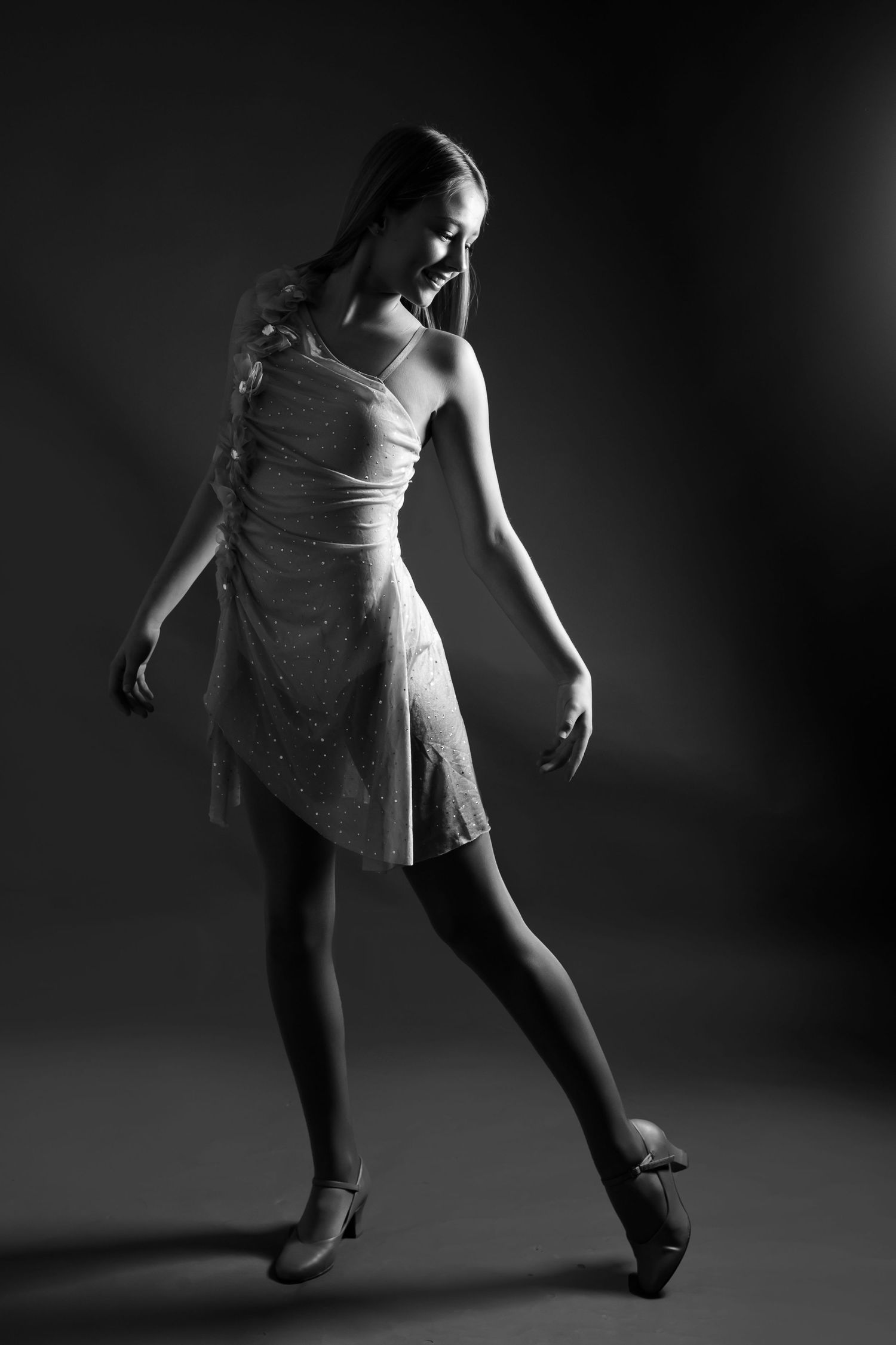 A dancer in a white dress performs an elegant pose in dramatic black and white lighting.