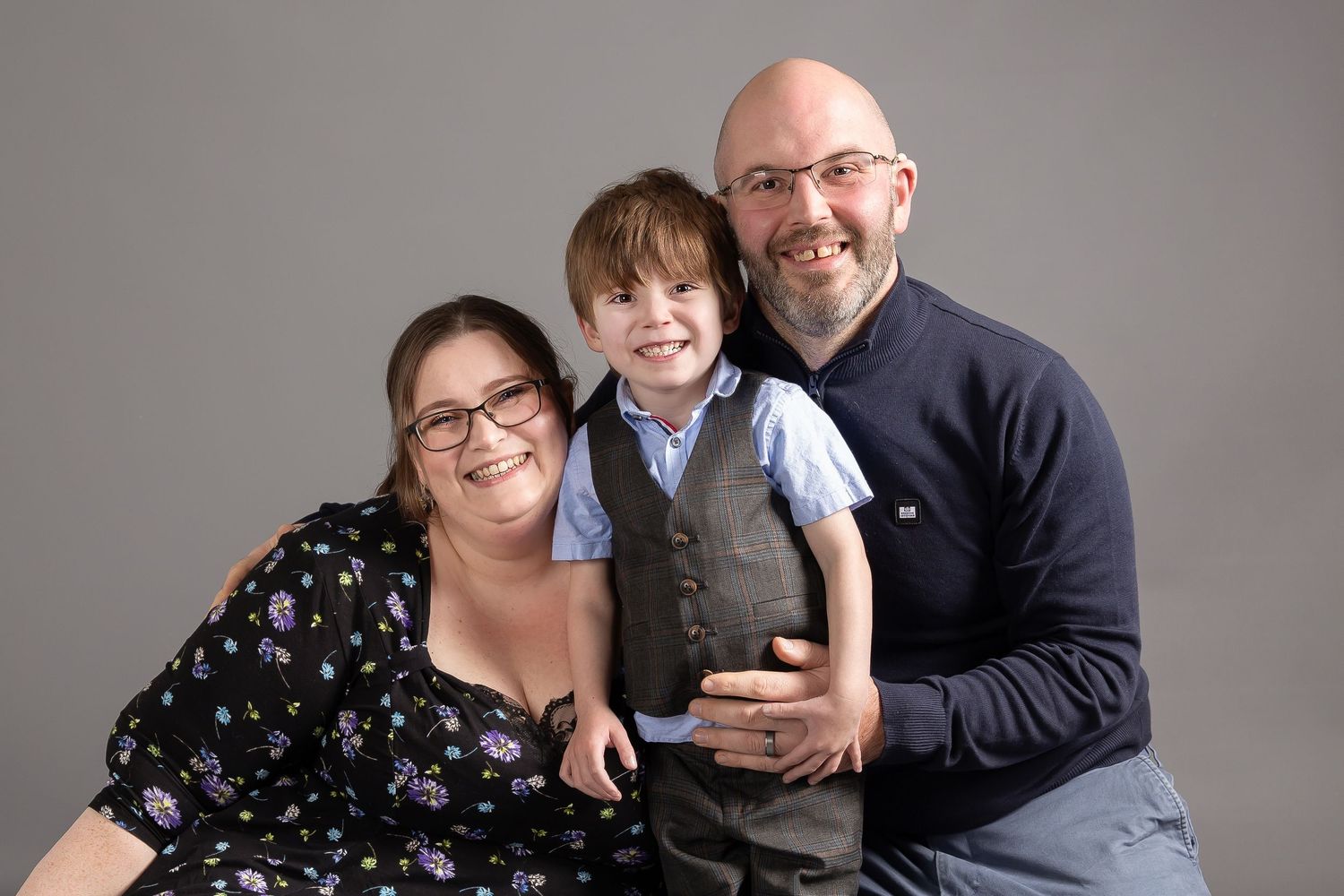 A happy family poses together against a gray studio backdrop while wearing semi-formal attire.
