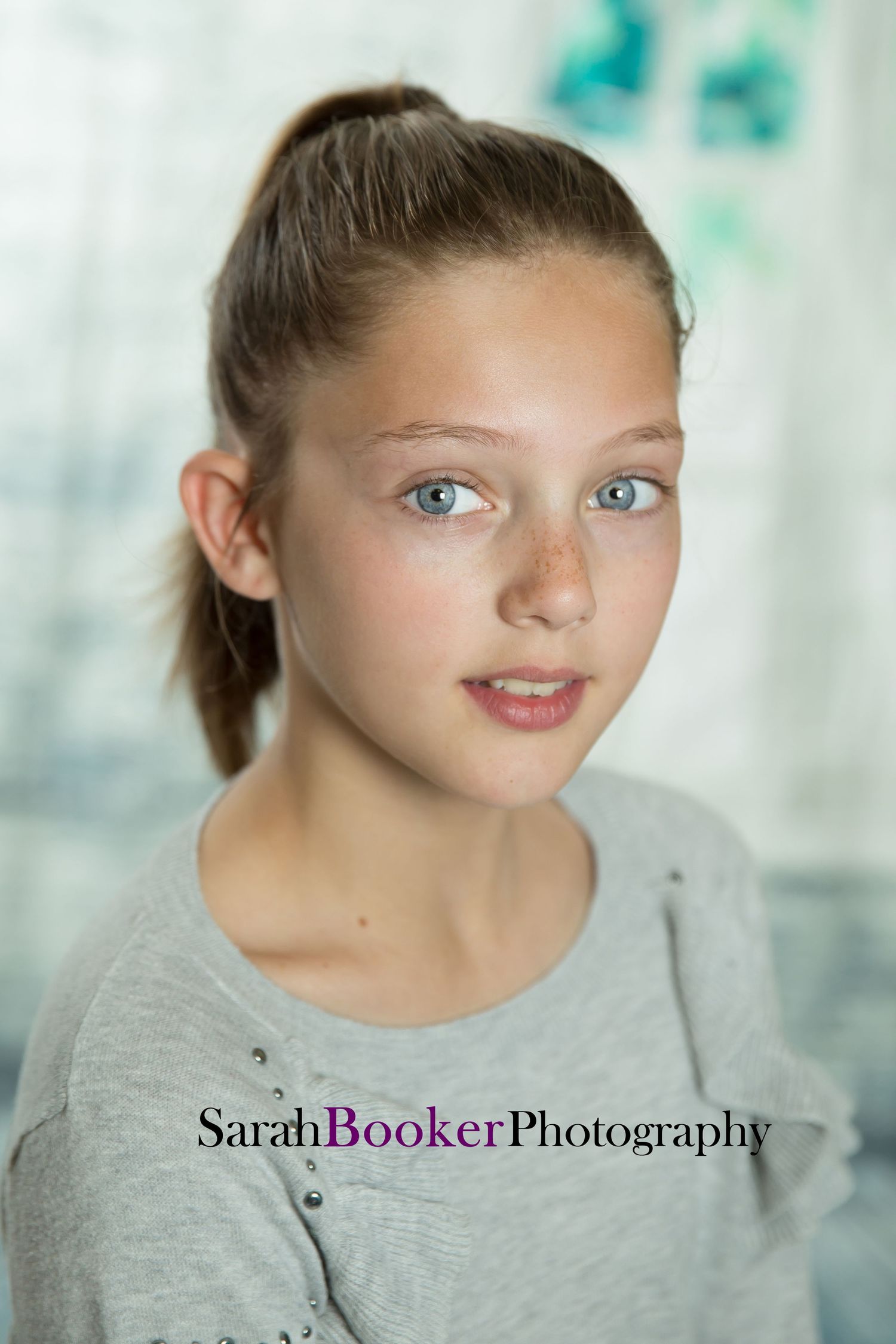 Studio portrait in natural light with a soft turquoise background and grey top showing gentle expression.