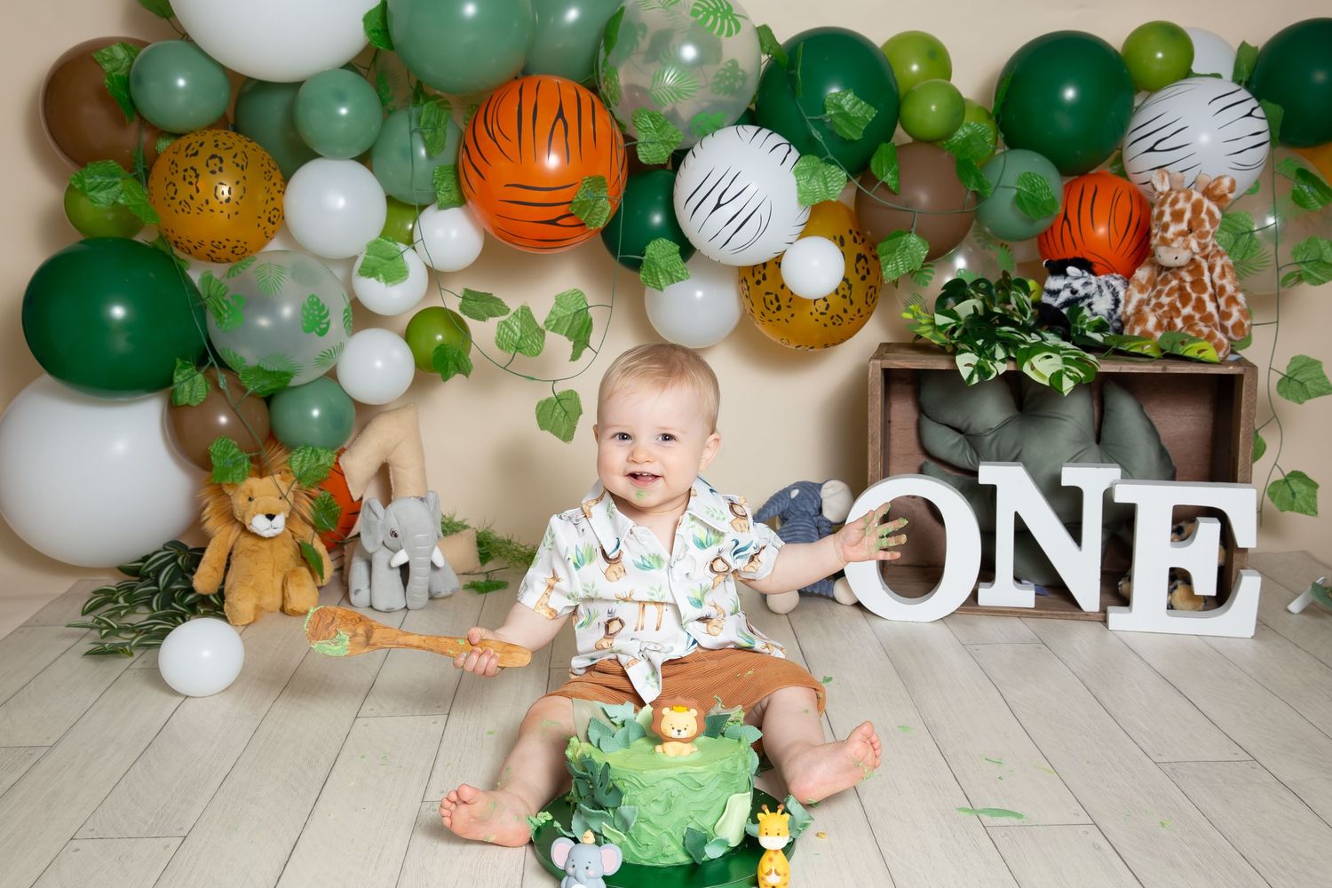 Green and white balloon decorations with woodland theme elements create a festive first birthday party backdrop.