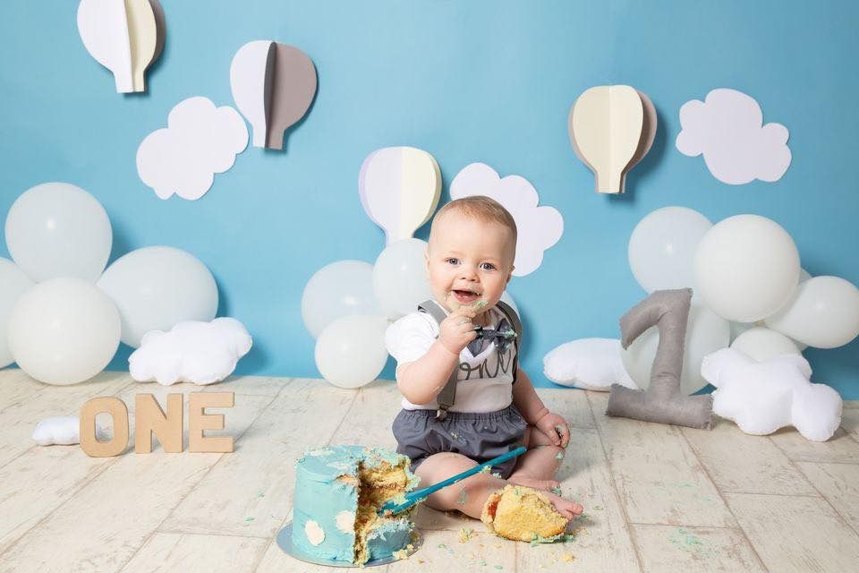 A series of baby milestone photos with cloud decorations and cake smash setup against a light colored backdrop.