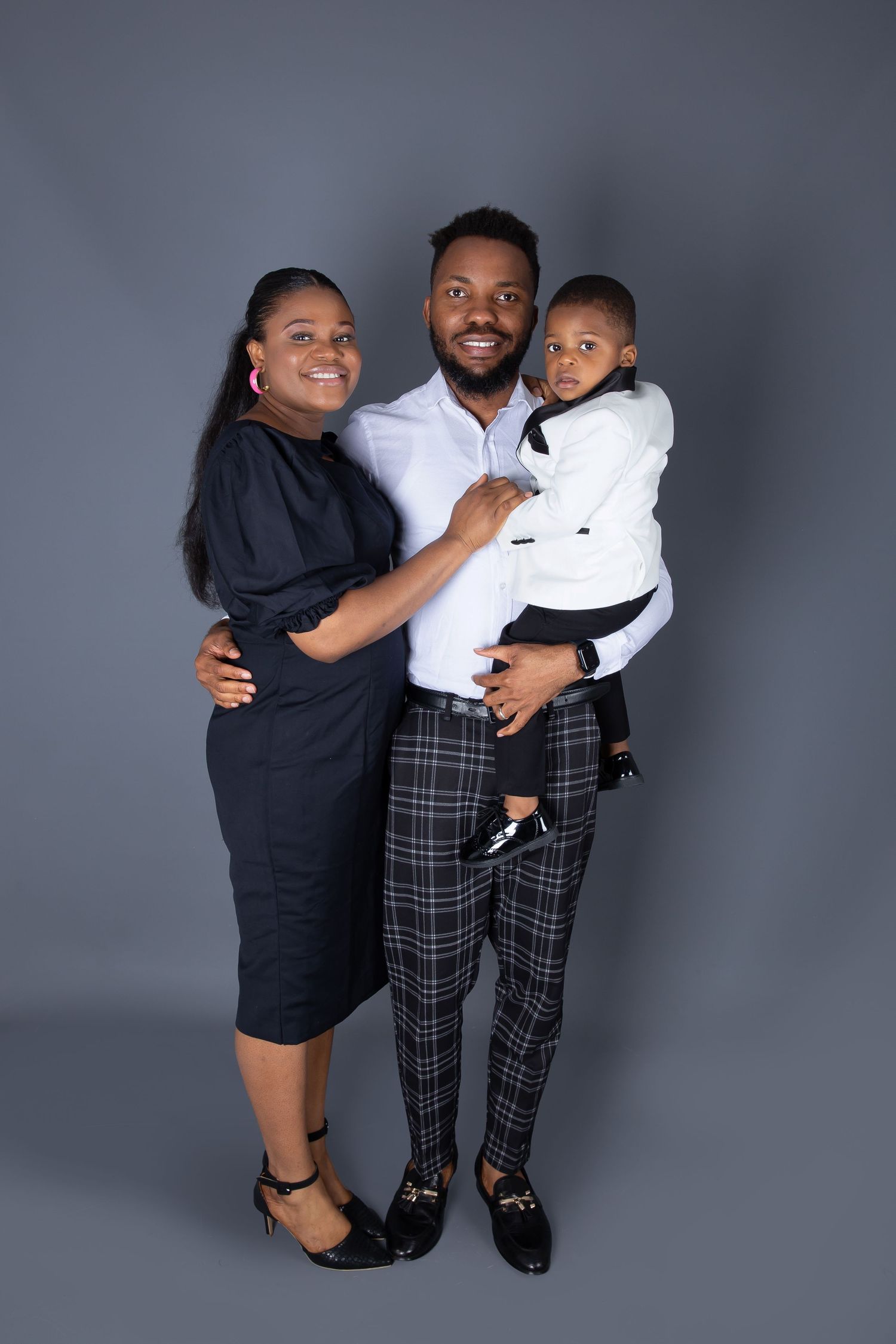 Stylish family wearing formal attire poses together for portrait against gray studio background.