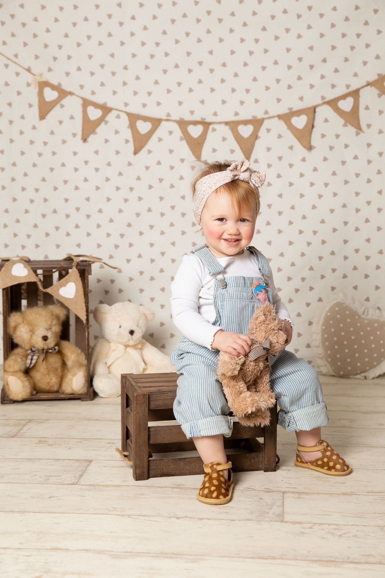 Sweet nursery scene with teddy bears, bunting banner, polka dot wallpaper, and small wooden stool on light wood flooring.