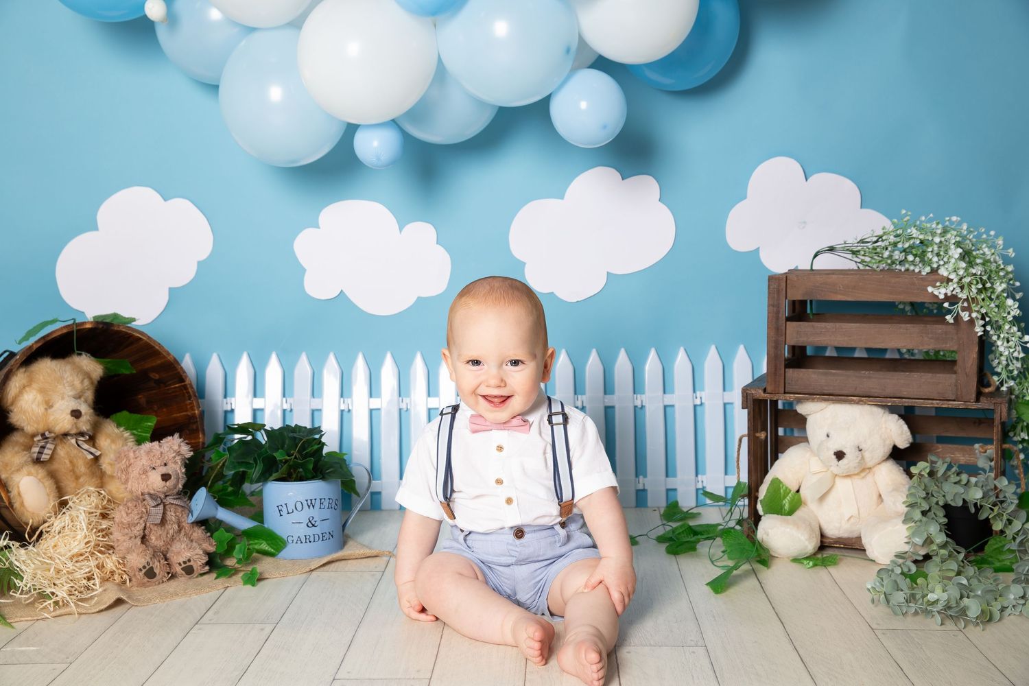Collage of baby photo studio setup with white clouds, picket fence, teddy bears and blue background decor pieces.