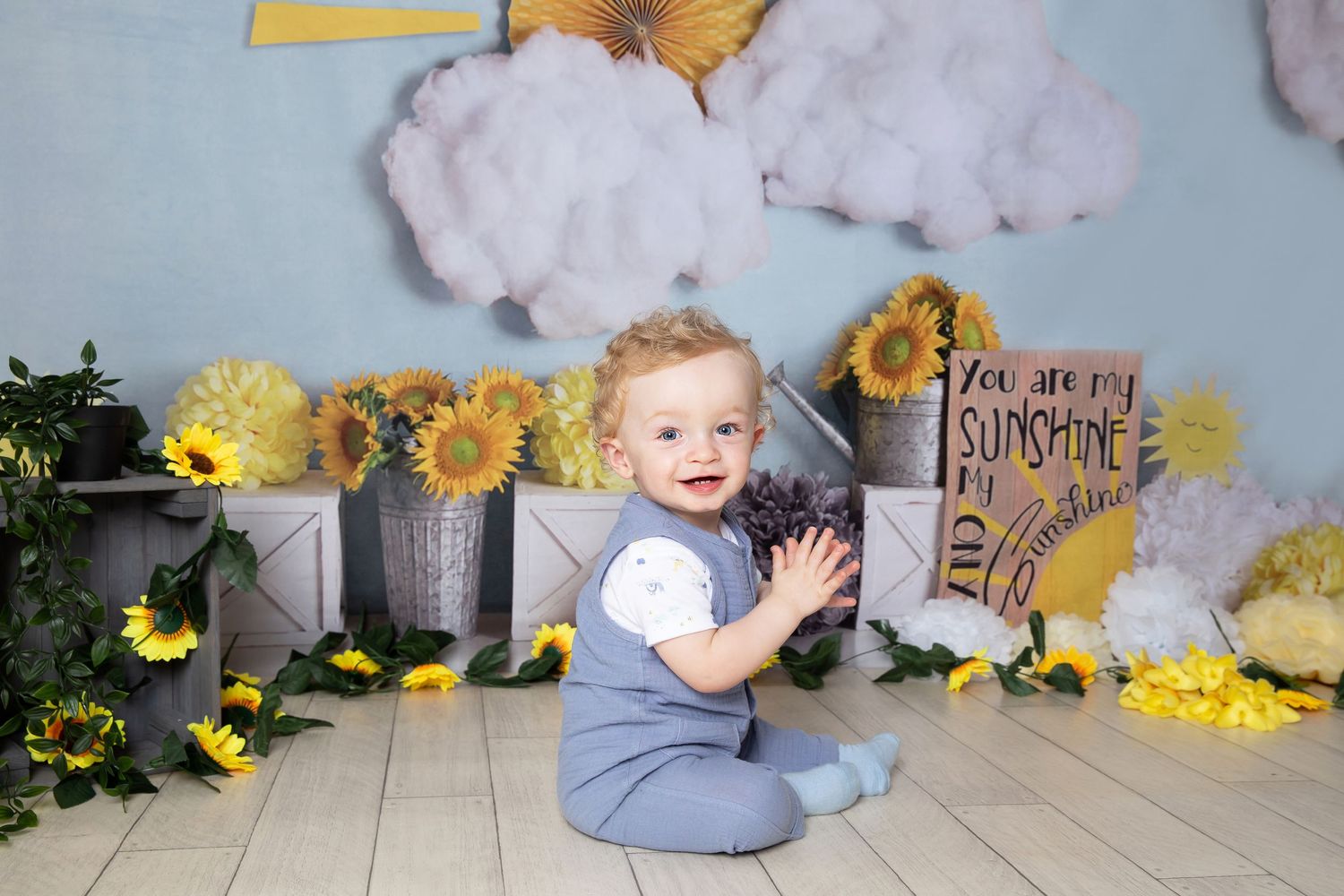 Charming nursery setup with sunflowers in galvanized buckets, fluffy cloud decorations, and rustic wooden sign.