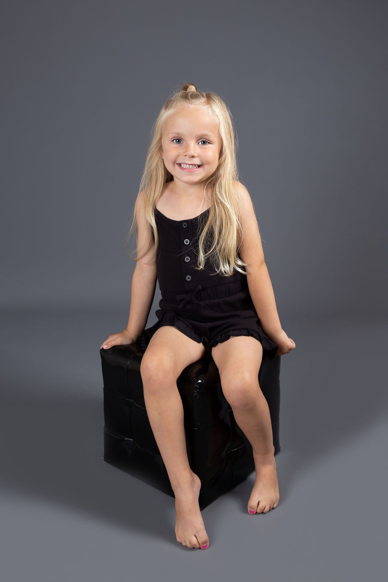 A series of studio portraits showing someone sitting in a casual pose against a dark gray background while wearing black.