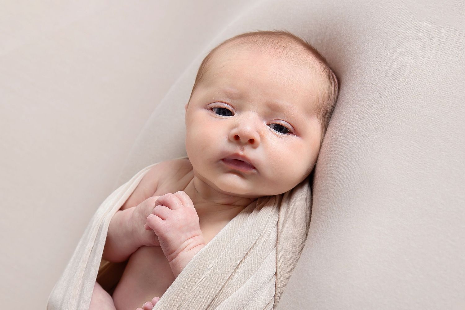 A baby in swaddling blankets lies on a soft bed with six candid expressions and poses side by side.