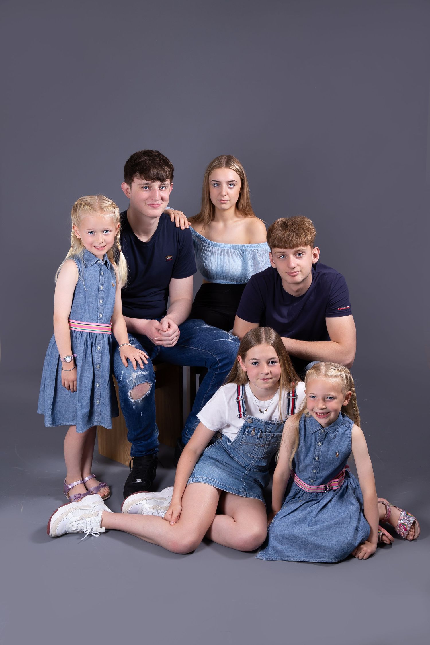 A group poses together wearing coordinated blue and navy outfits against a gray studio background.