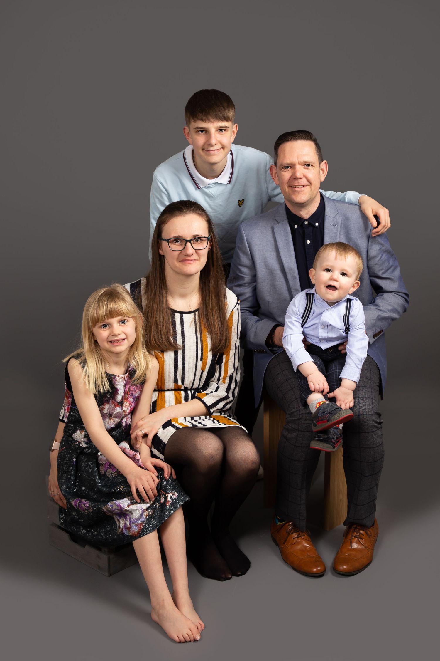 A series of four family studio portraits with adults and children in formal attire against a grey background.