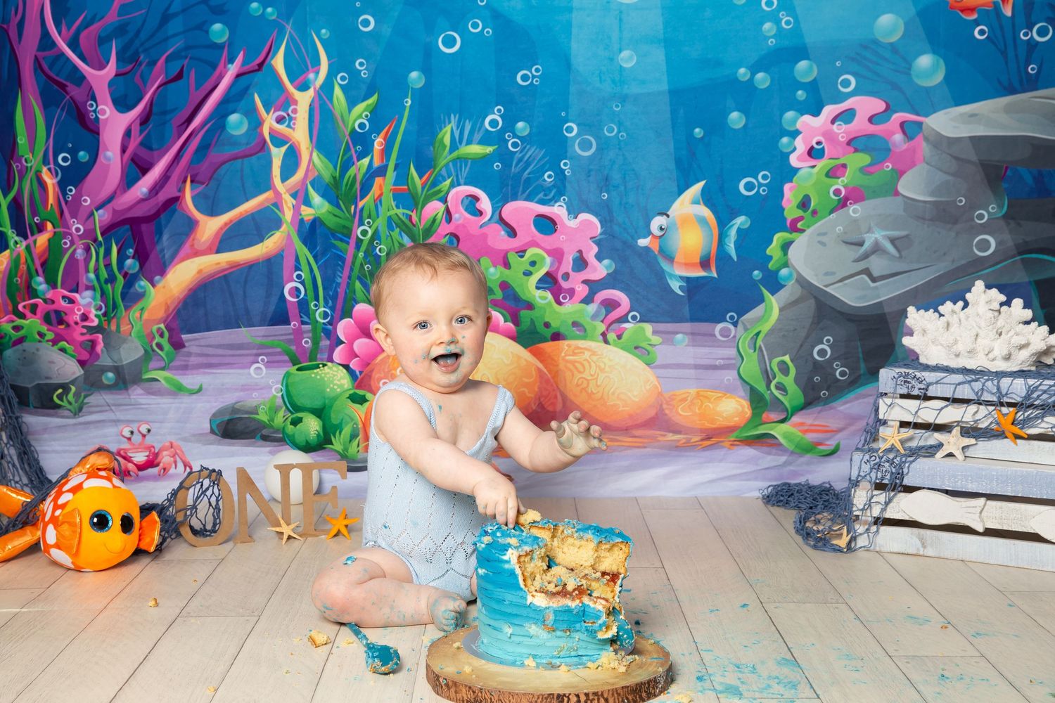 Colorful underwater themed birthday party setup with cake, decorations, and toys against a blue backdrop.