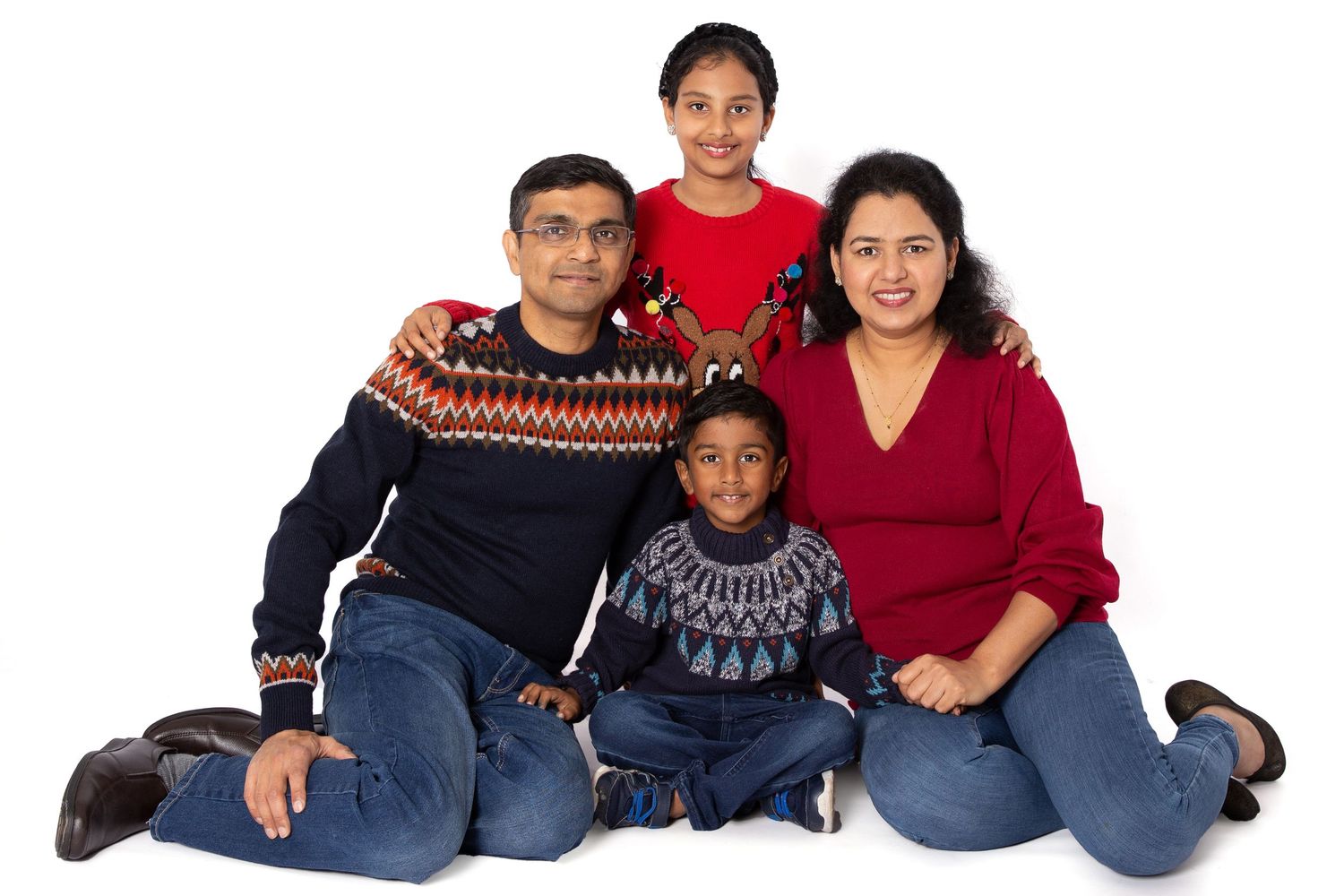 Family of five wearing coordinating winter sweaters sitting together on white background for portrait.