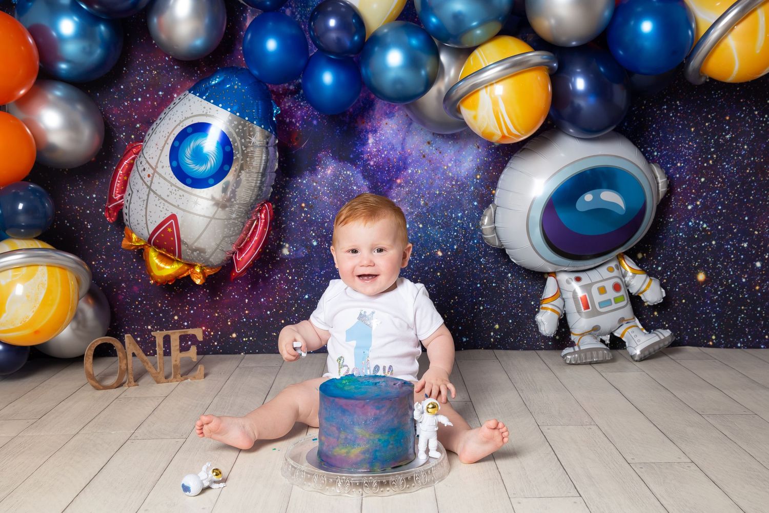 A space-themed photo backdrop with silver and blue balloons creates a cosmic atmosphere for a baby photography session.