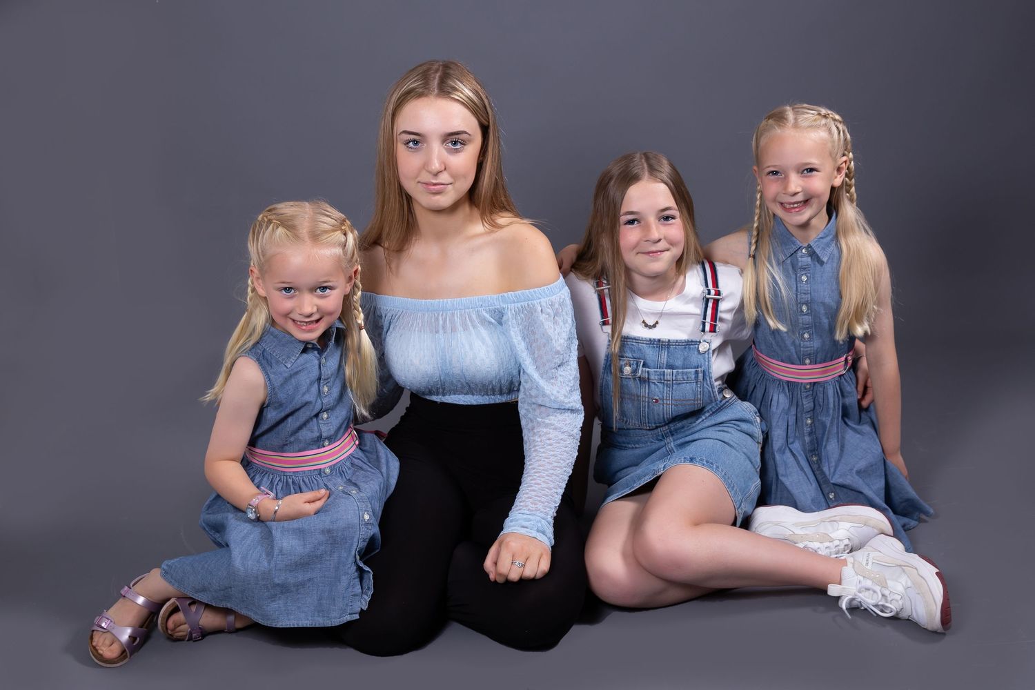 A group poses together in casual attire against a dark gray studio background for a family portrait session.