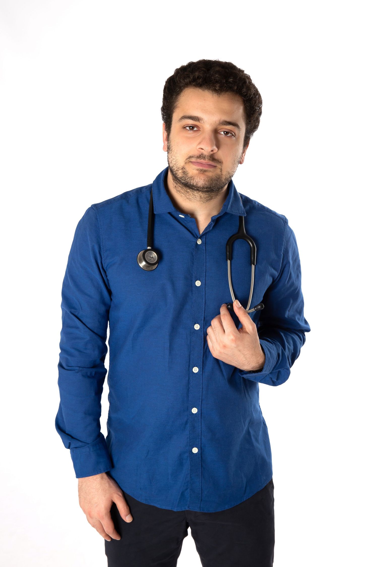 A medical professional in a blue button-down shirt with a stethoscope around their neck stands against a white background.