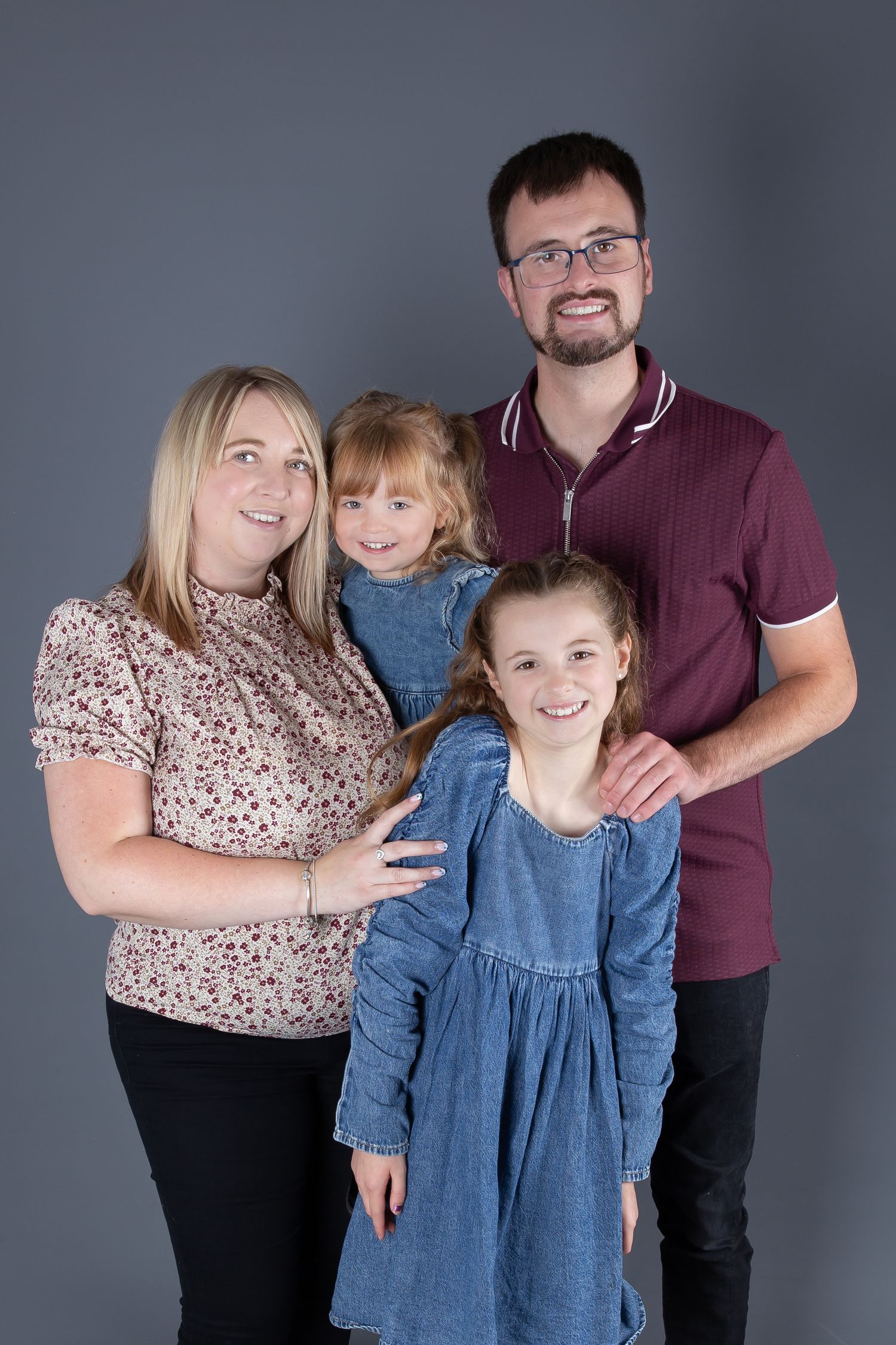 Studio portrait of a family of four posing together against a grey background.