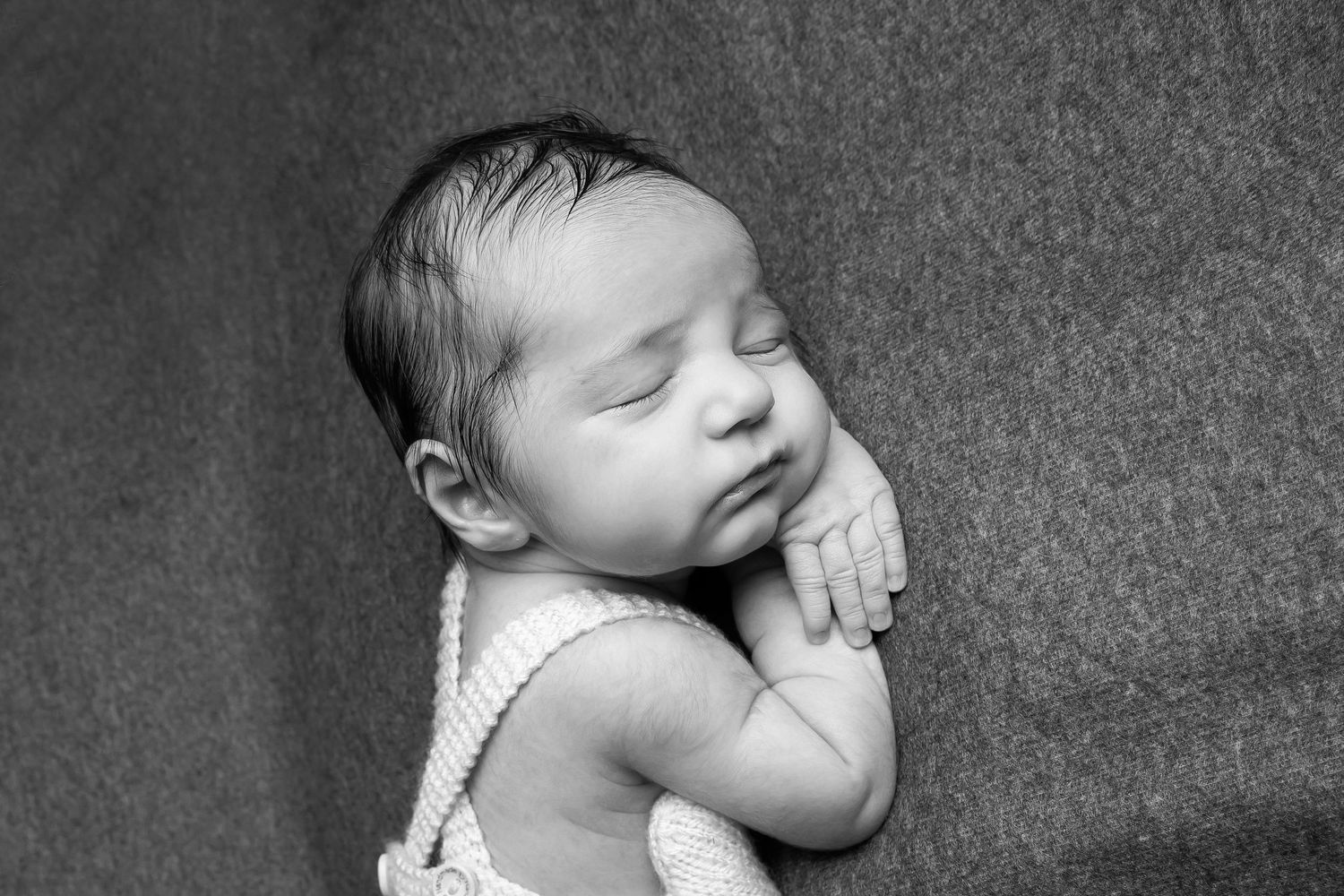 Black and white portrait of a sleeping newborn baby with hands tucked under chin resting on soft blanket.