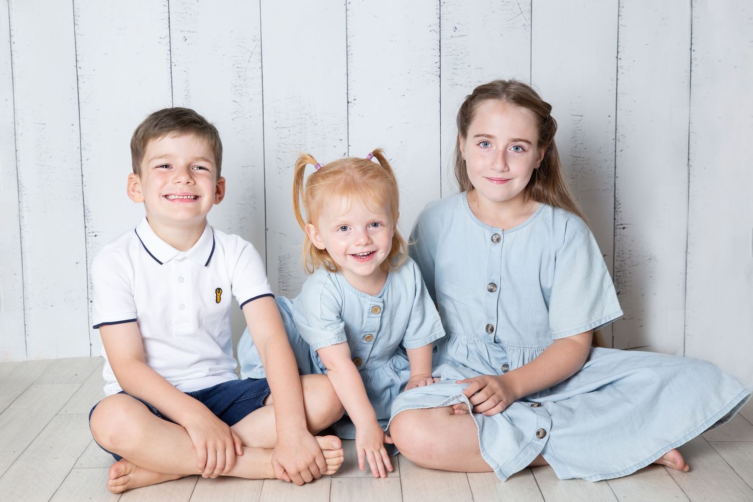 A group wearing matching light blue outfits sits together on a white backdrop for a casual family photo session.