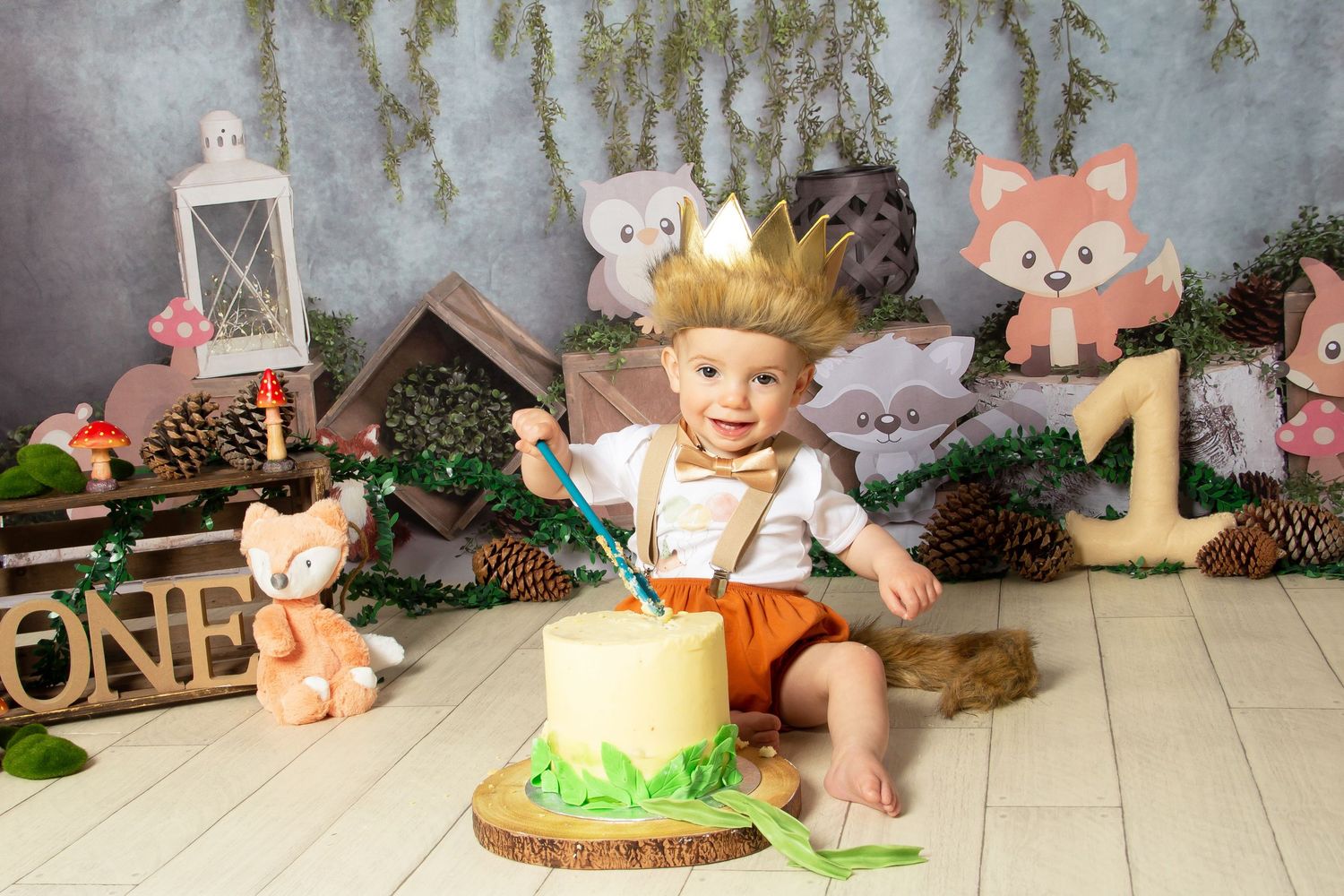 Woodland themed first birthday cake smash setup with rustic decorations, lantern, forest animals and number one sign.