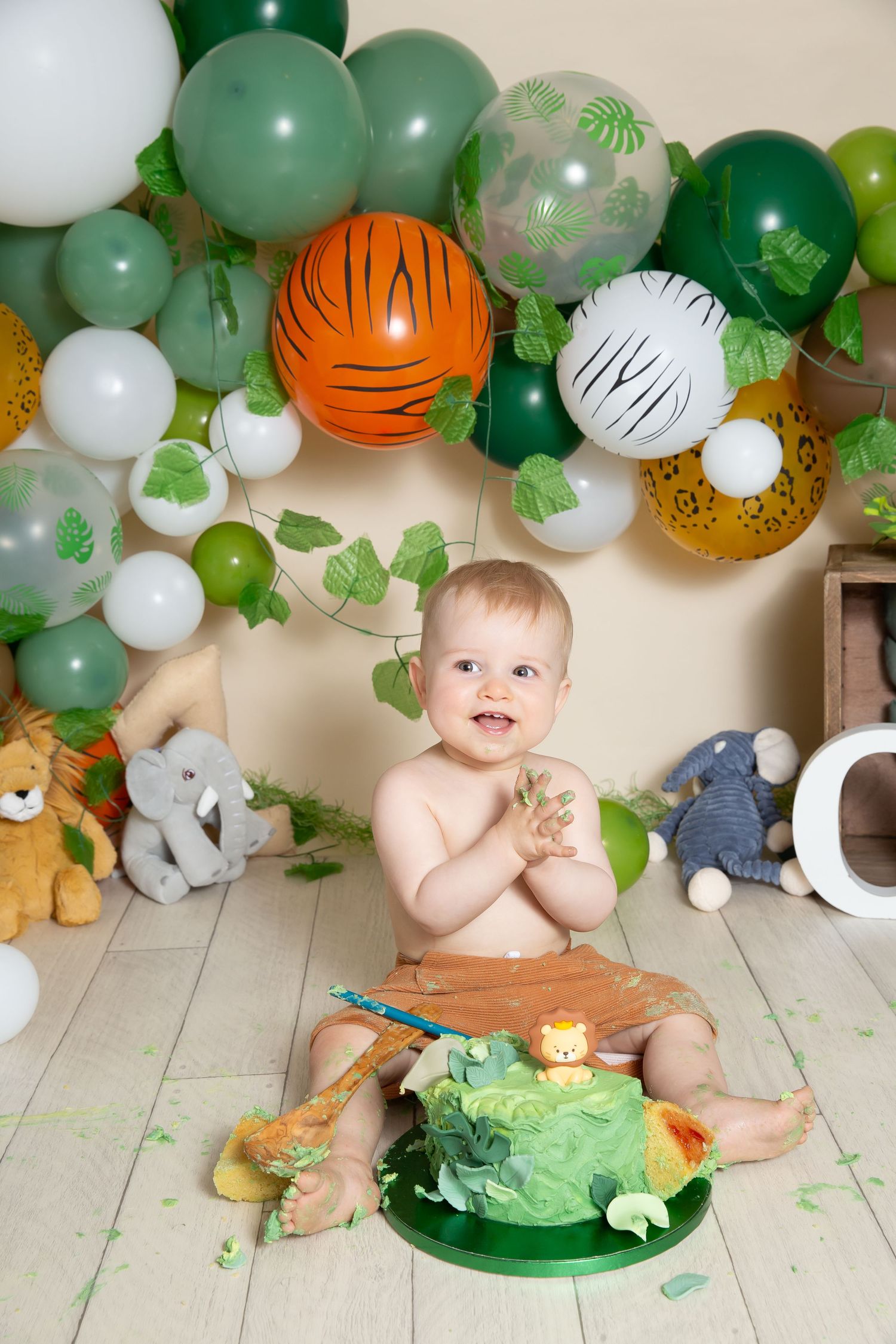 Festive jungle-themed birthday setup with green balloon arch, safari animal plush toys and colorful decorative elements.