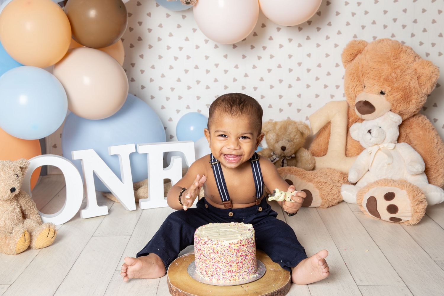 First birthday celebration setup with balloons, teddy bears, and a cake against a polka dot backdrop.