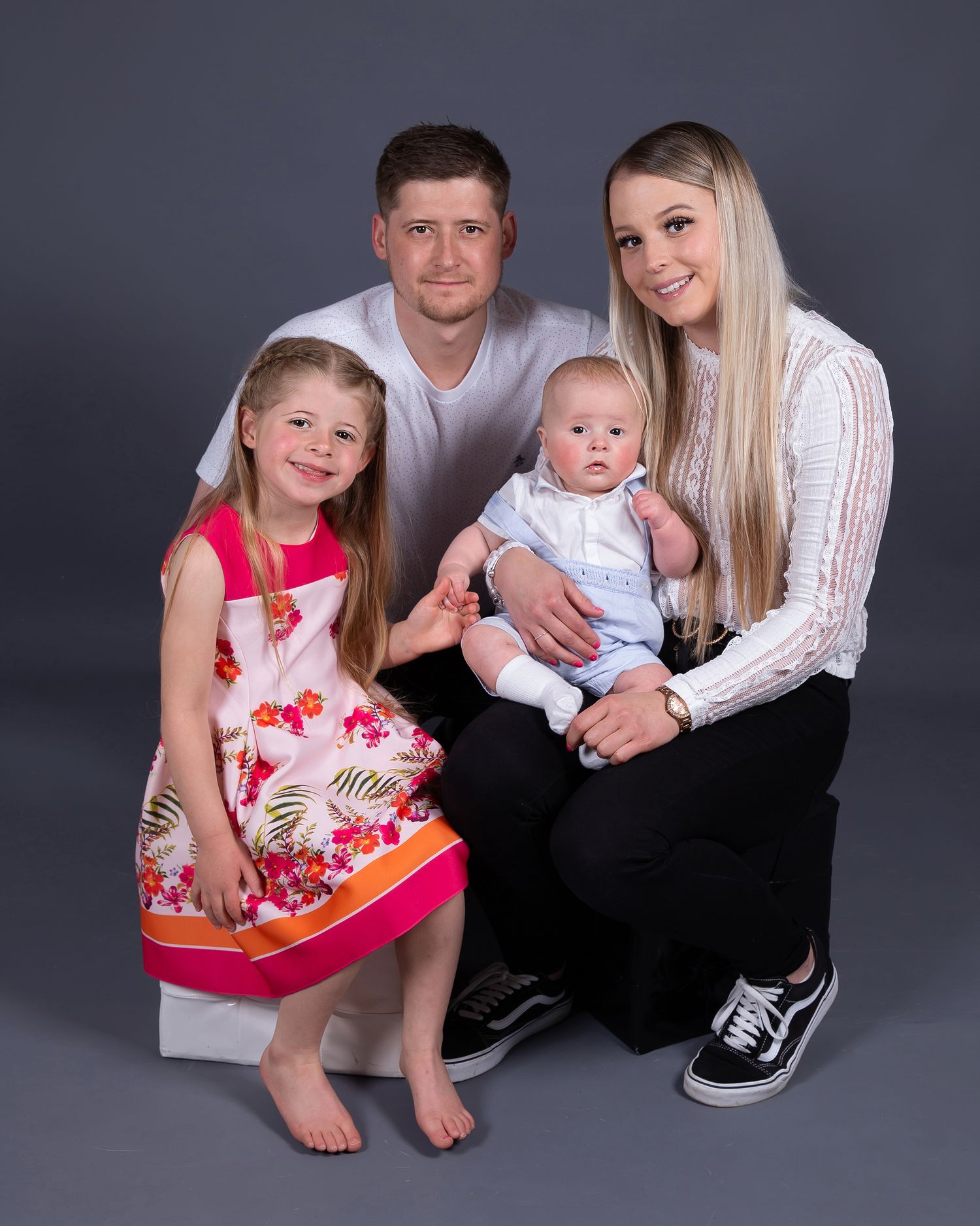 Family portrait of parents with two children posing together on a gray background.