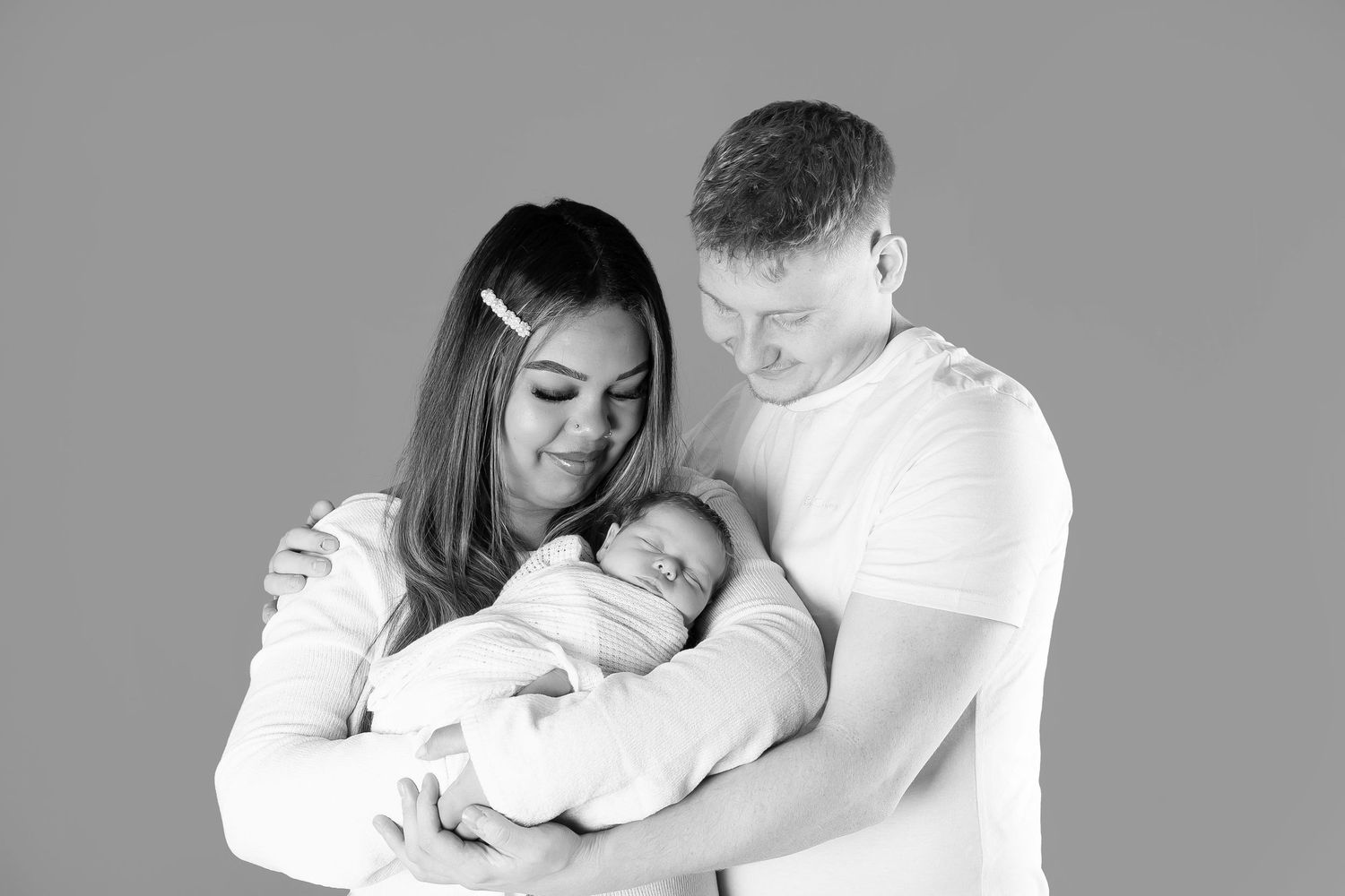 Black and white photo series showing parents tenderly holding and bonding with their sleeping newborn baby.