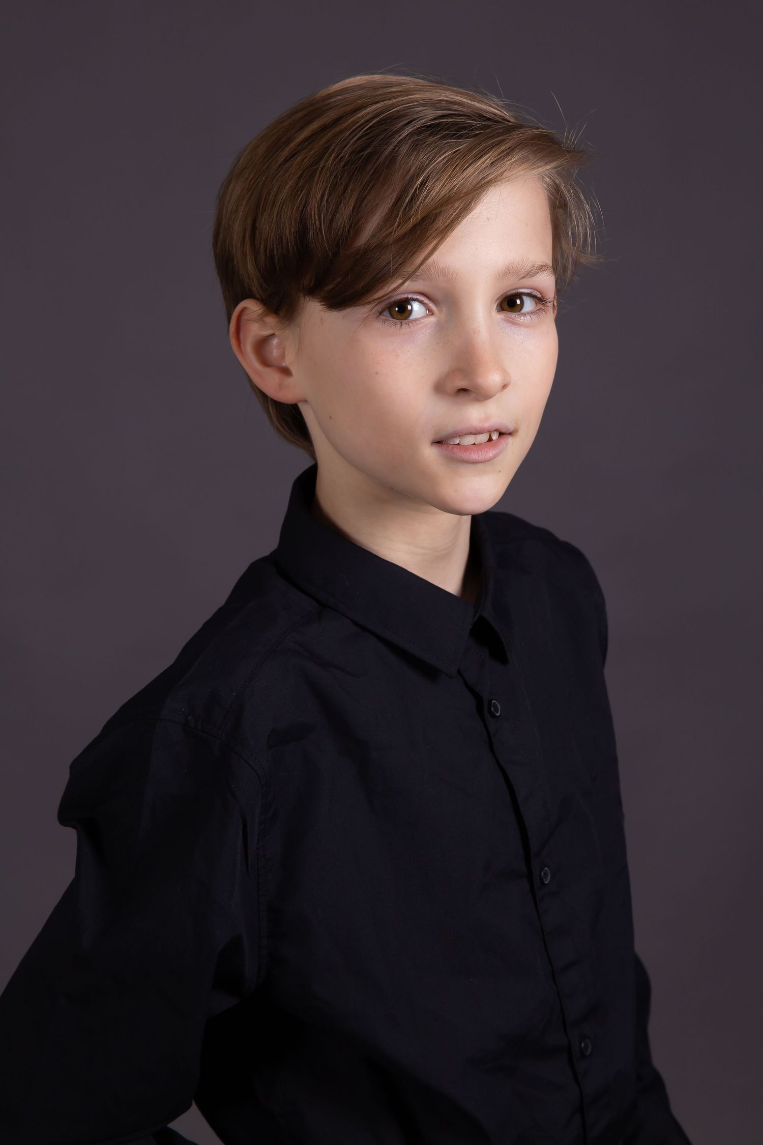 Studio portrait of a young person in a black button-up shirt against a dark background.