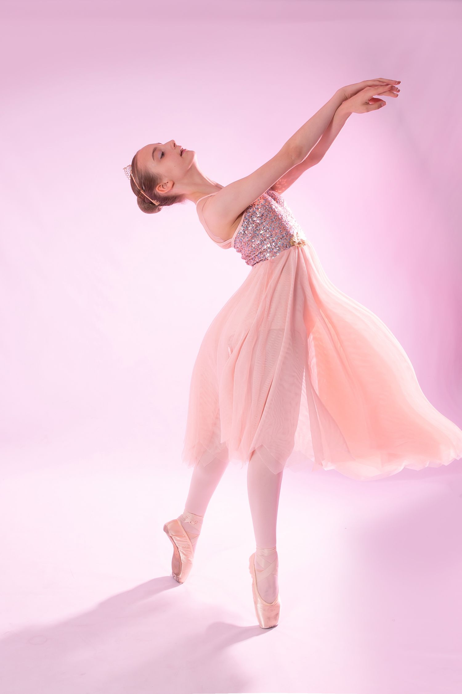 Ballerina in pink tutu and pointe shoes strikes graceful pose on pink background.